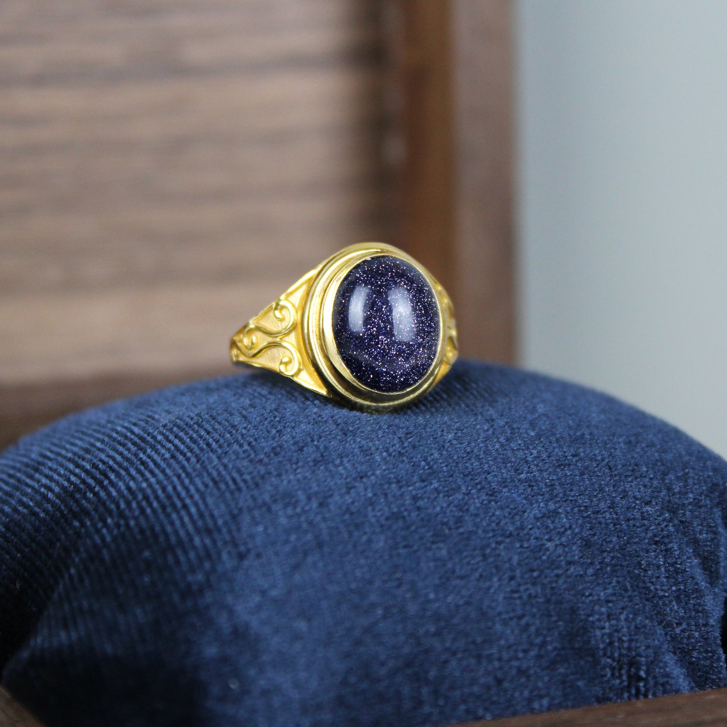 Gold night keeper signet ring with a deep blue sandstone gemstone on a blue cushion