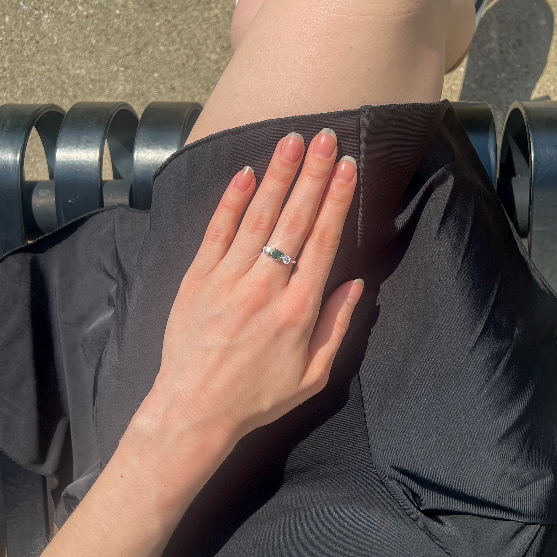 Edwardian Three Stone sterling silver ring on model hands held on lap in black dress, green CZ center stone, Ether Jewelry