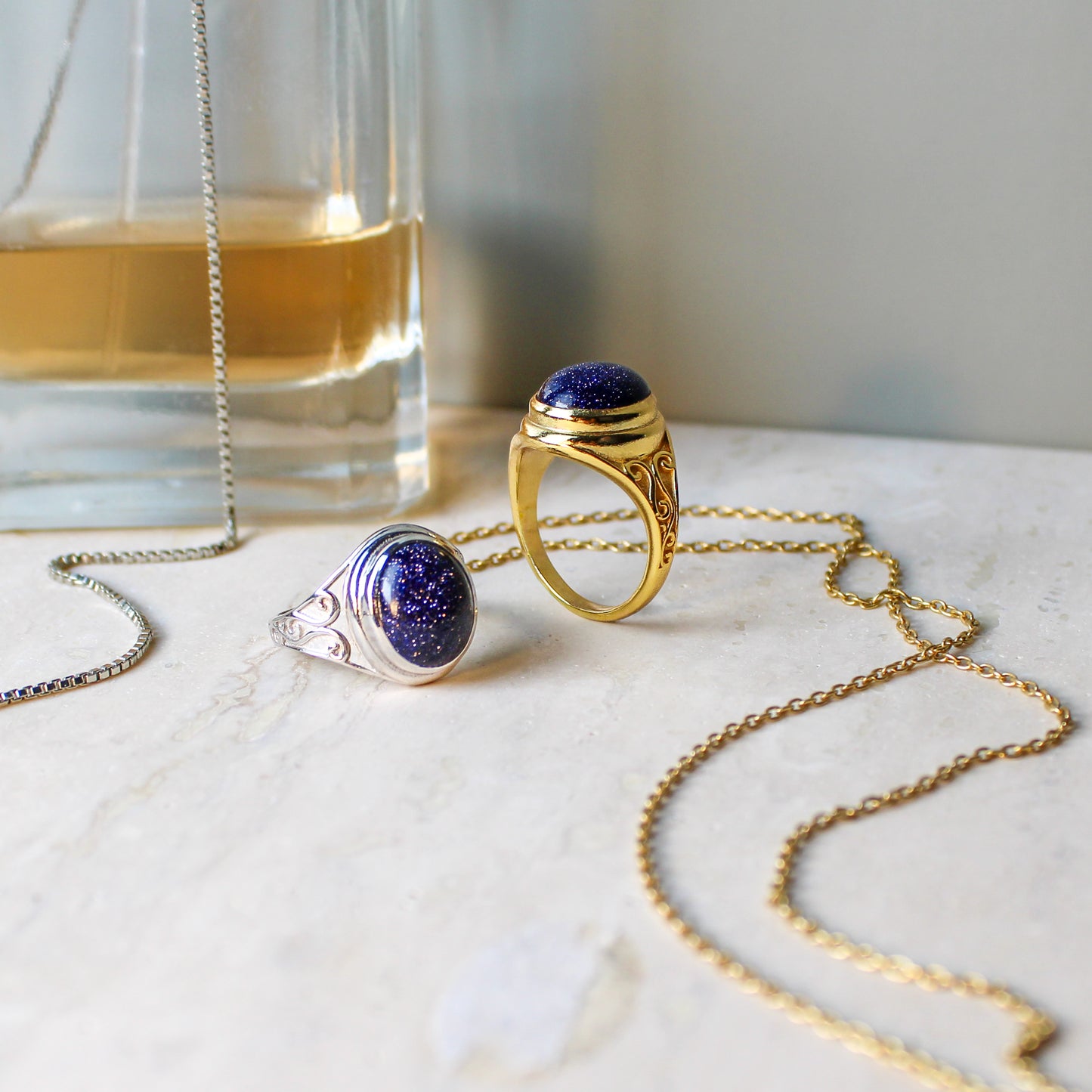 Night Keeper Ring 18k gold vermeil staged next to perfume bottle and necklace chains with matching ring, blue sandstone signet jewelry, Ether Jewelry