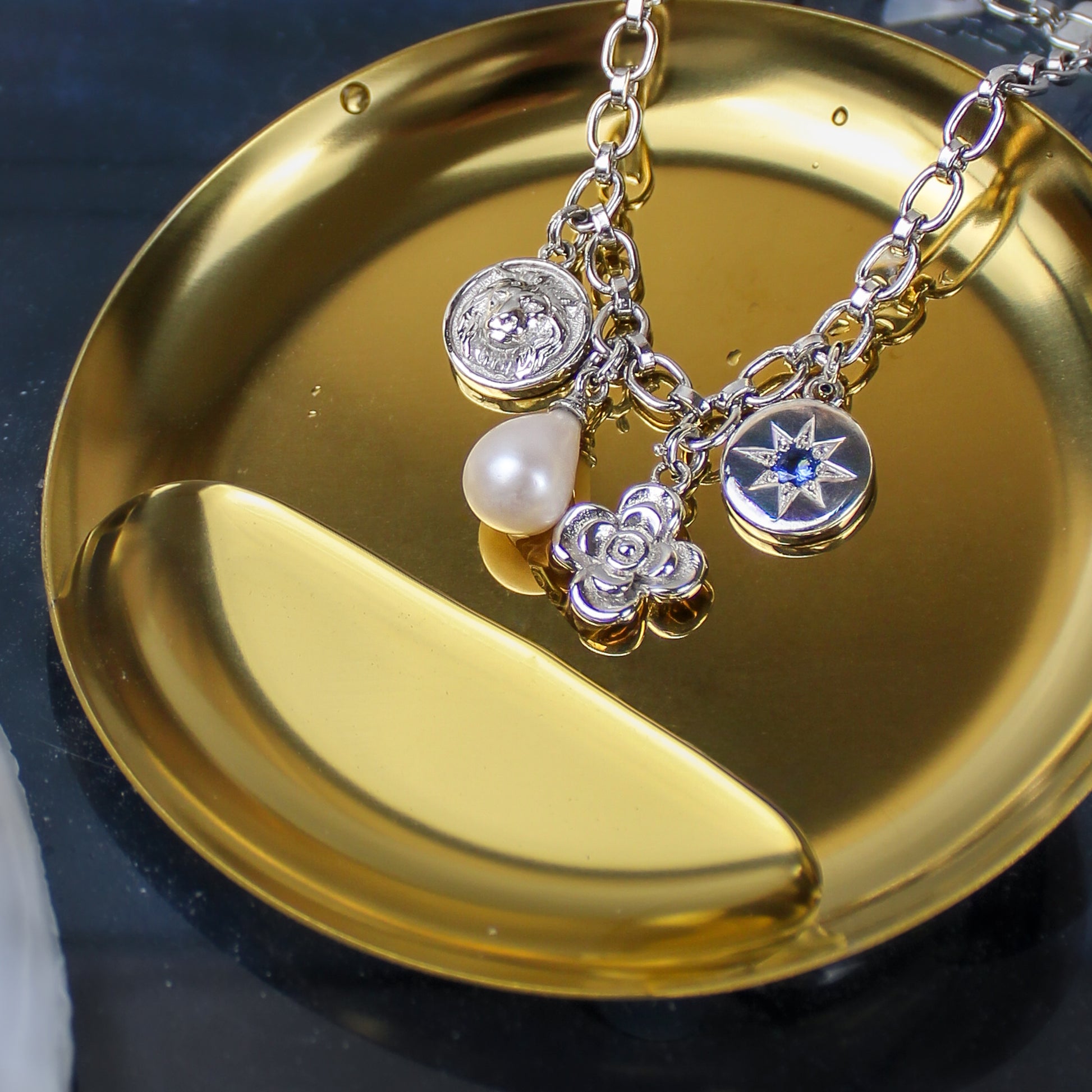 Archivist Bracelet in sterling silver on gold dish in water, lion coin pearl flower and north star charm bracelet, Ether Jewelry