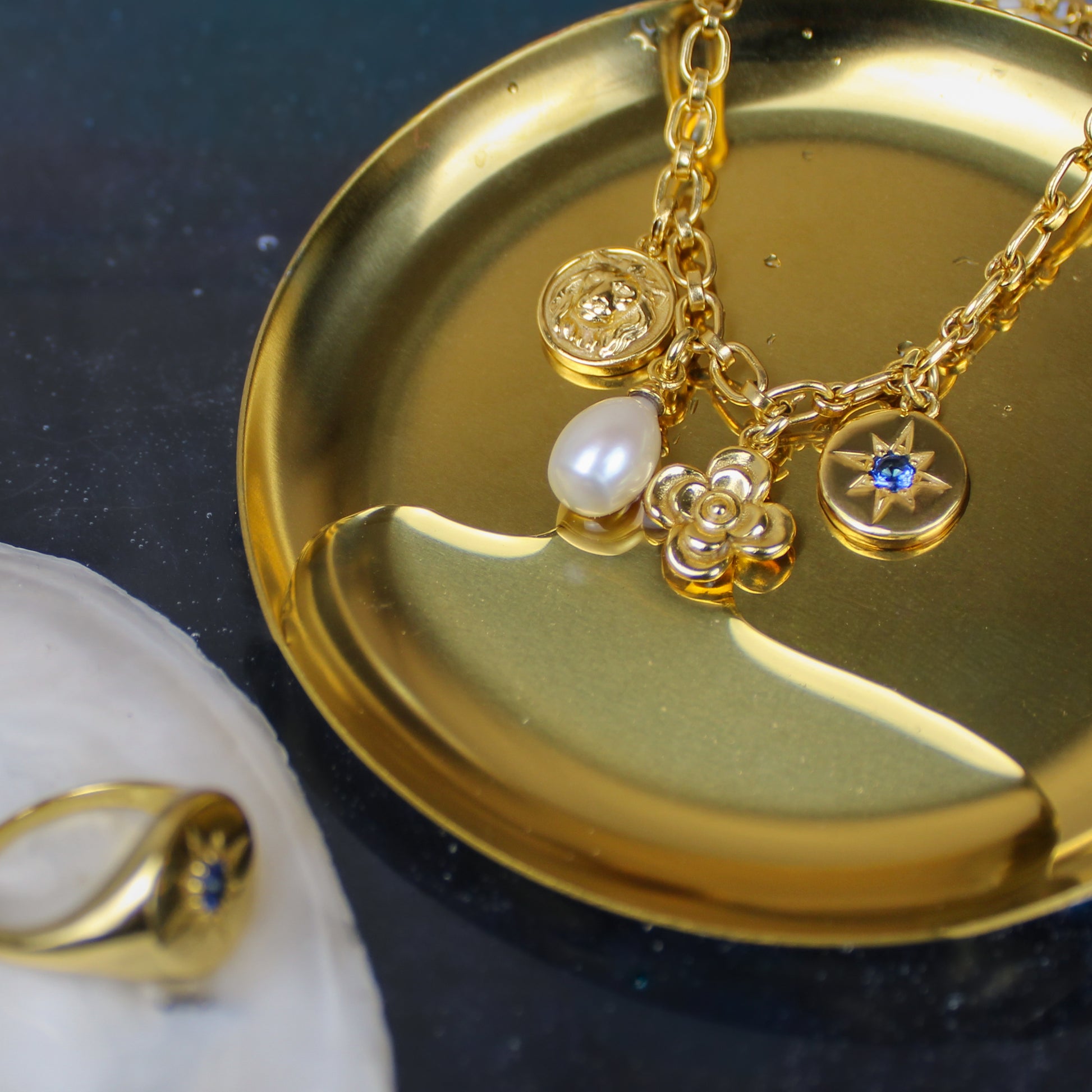Gold archivist bracelet with charms on a gold dish against a water background