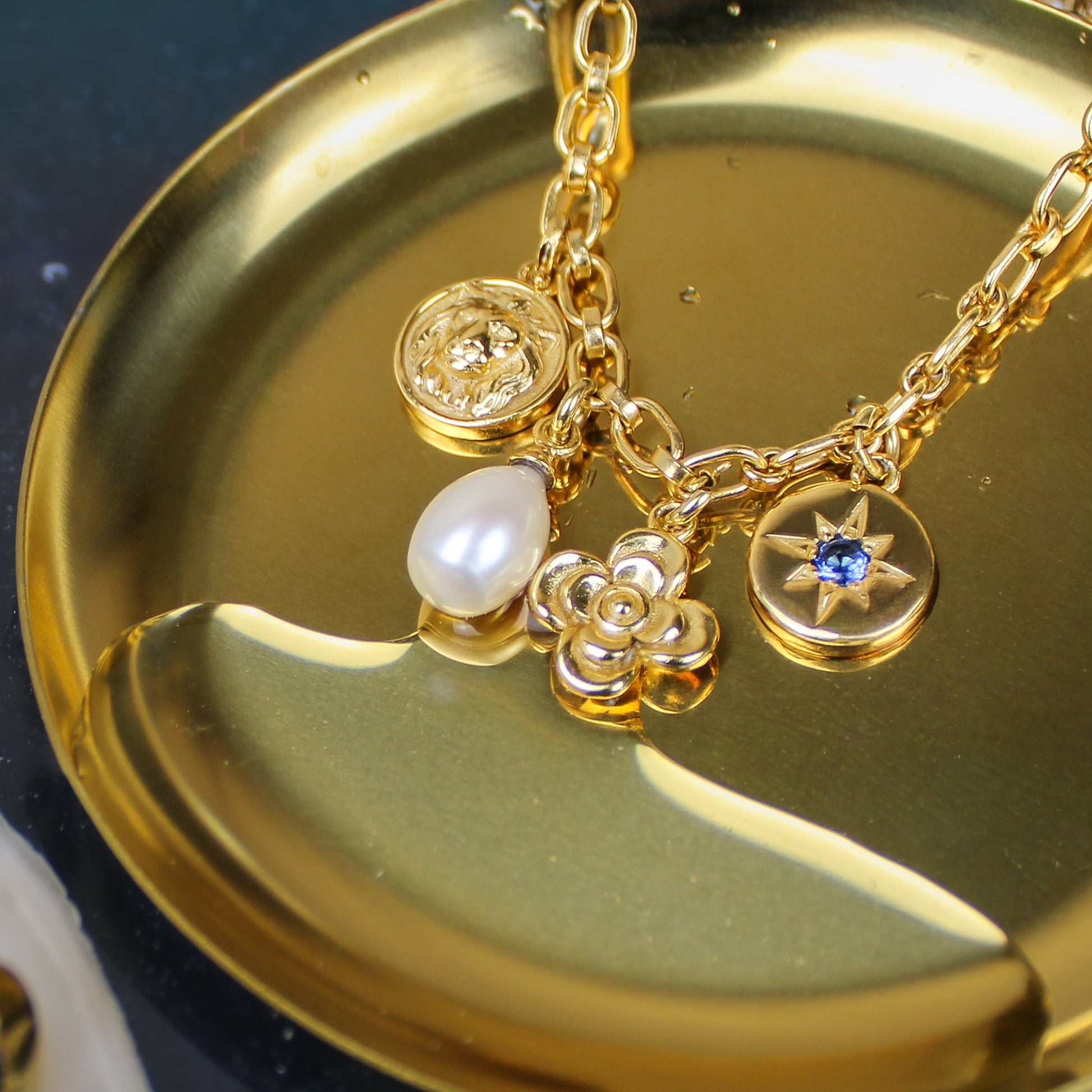 Archivist Bracelet in 18k gold vermeil on gold dish in water, lion coin pearl flower and north star charm bracelet, Ether Jewelry