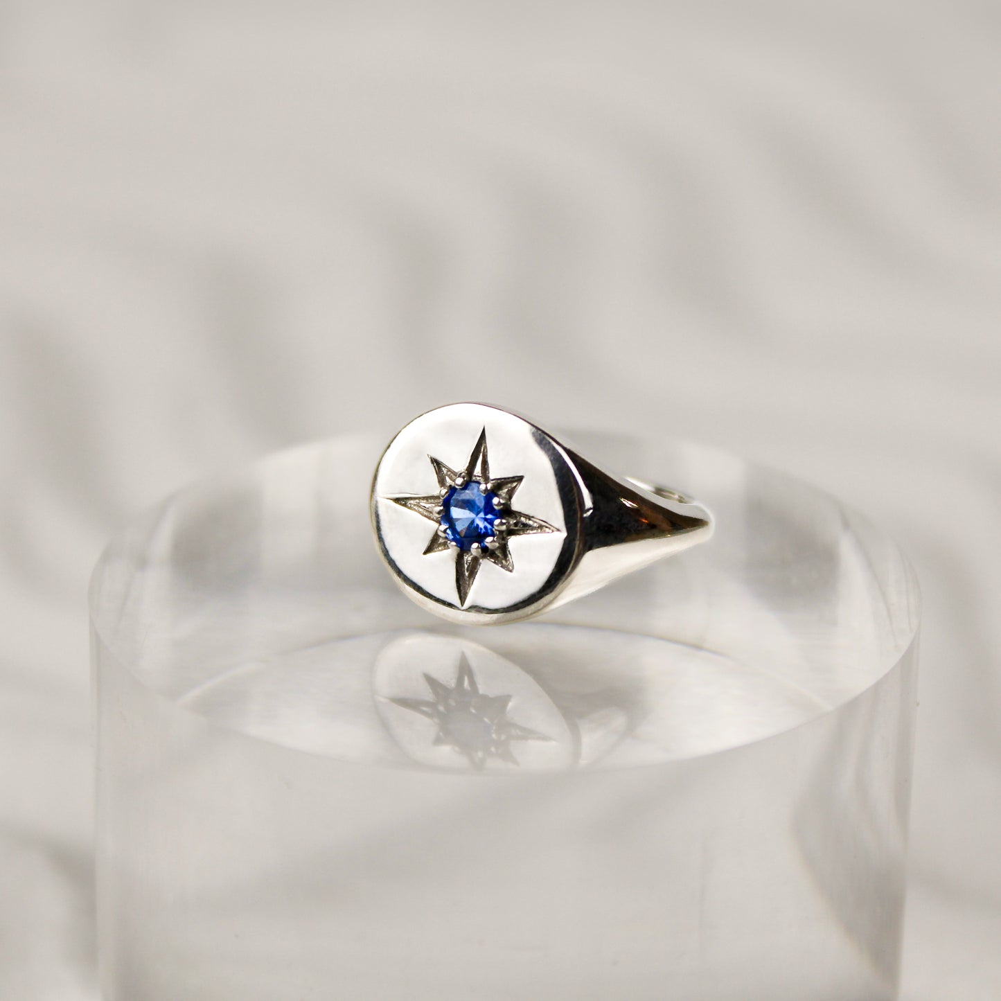 Sterling Silver Wayfinder signet ring with a blue gemstone and star engraving on a white sand background