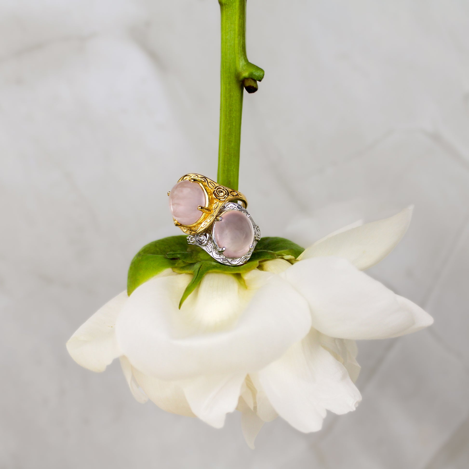 Gold and Silver romantic heir signet Rings with pink quartz gemstone and flower engravings on a white flower against a light gray background