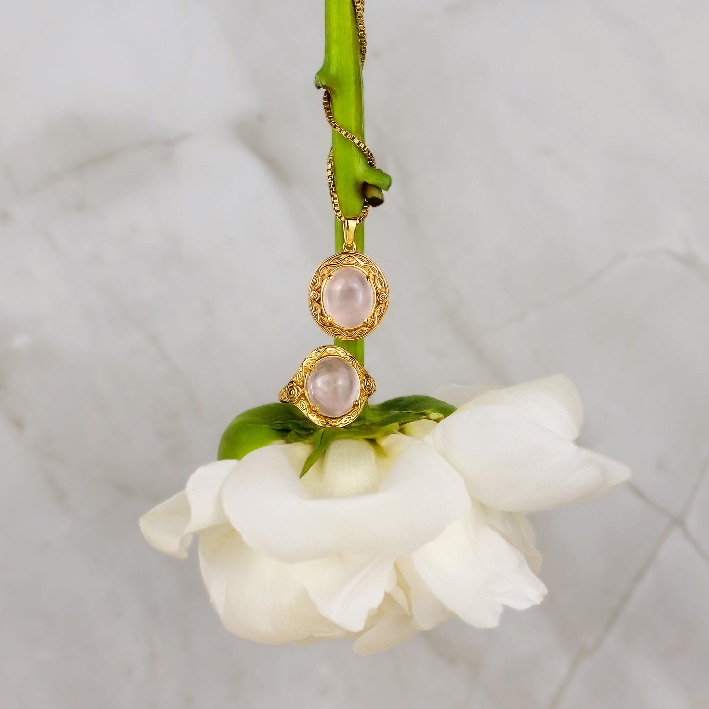 Gold romantic heir signet ring and necklace with pink quartz gemstones and flower engravings on a white flower stem against a light background