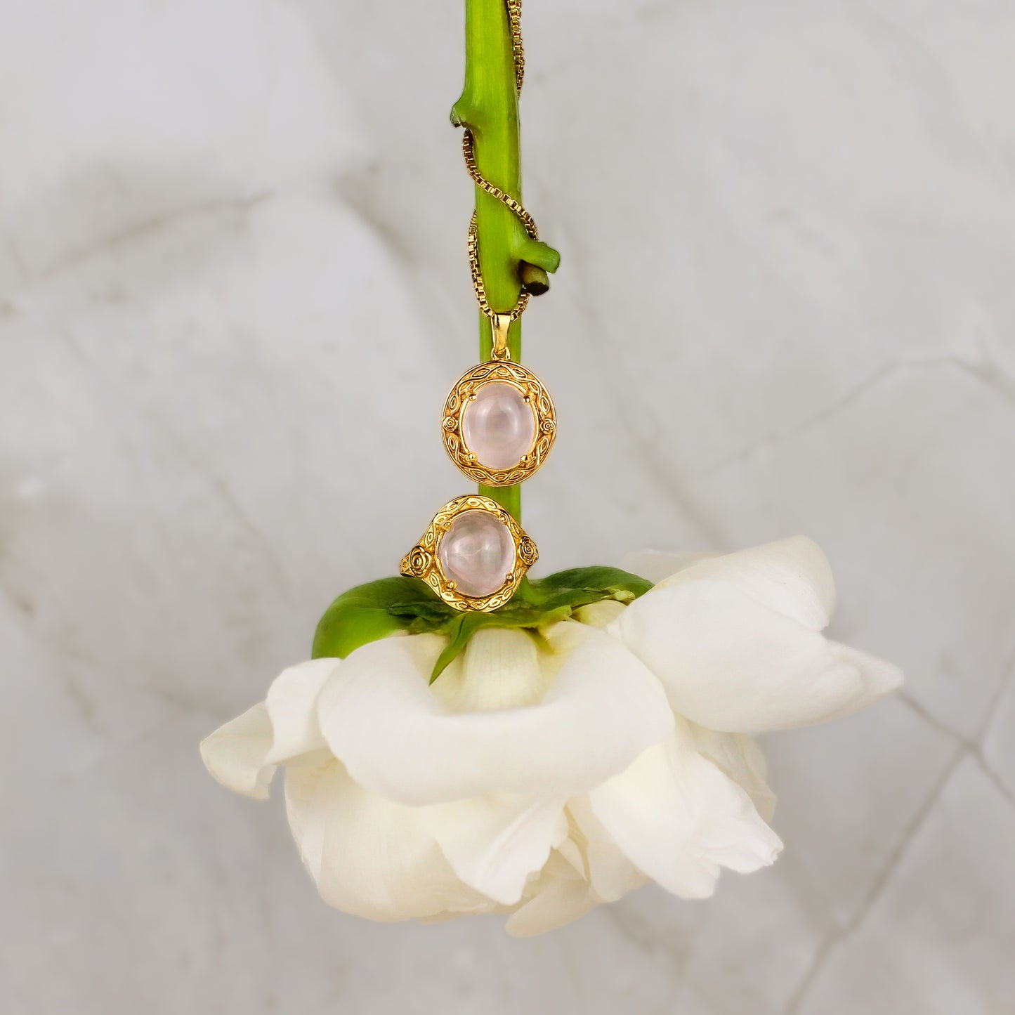 Gold Romantic Heir necklace and ring with pink gemstones on a white flower against a marble background