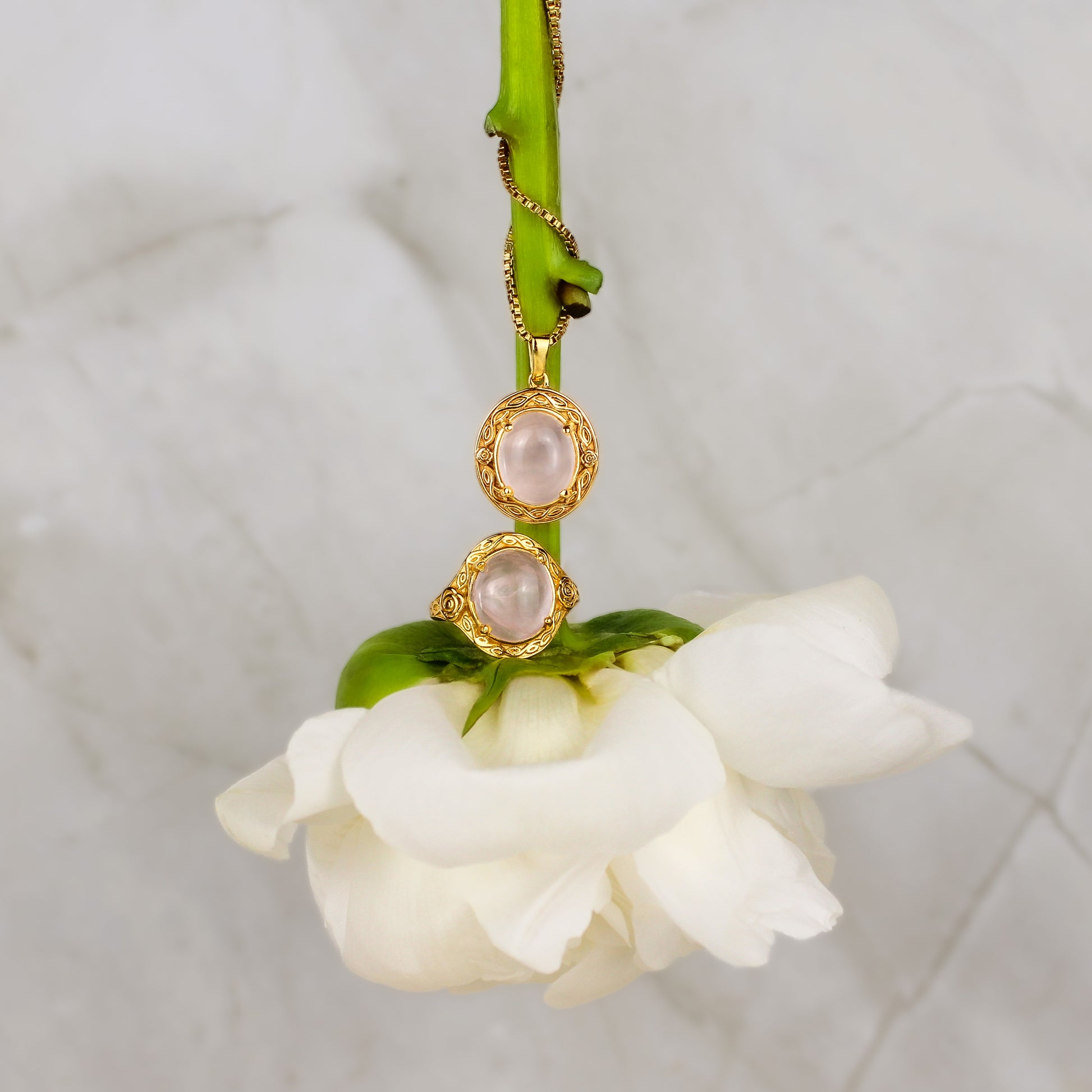 Gold Romantic Heir necklace and ring with pink gemstones on a white flower against a marble background