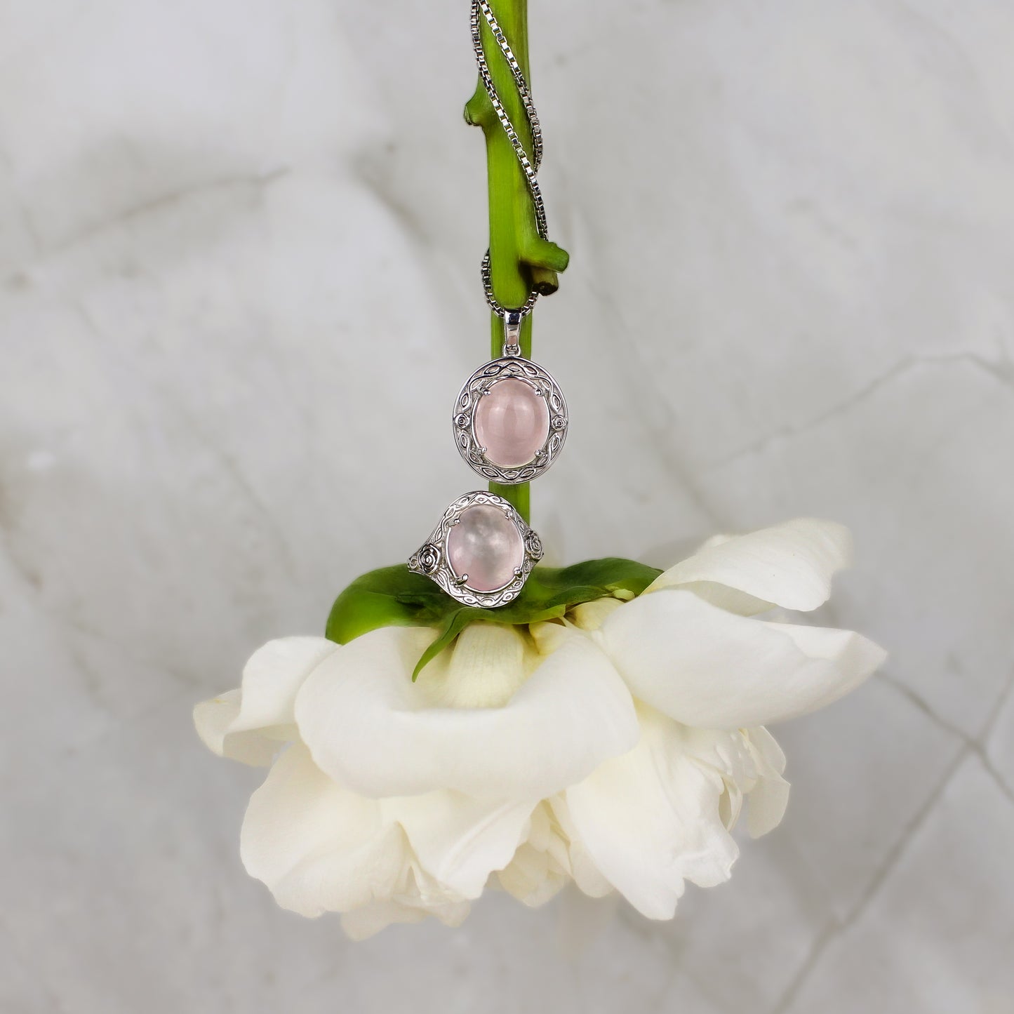Romantic Heir Necklace and ring with pink gemstones on a white flower against a marble background
