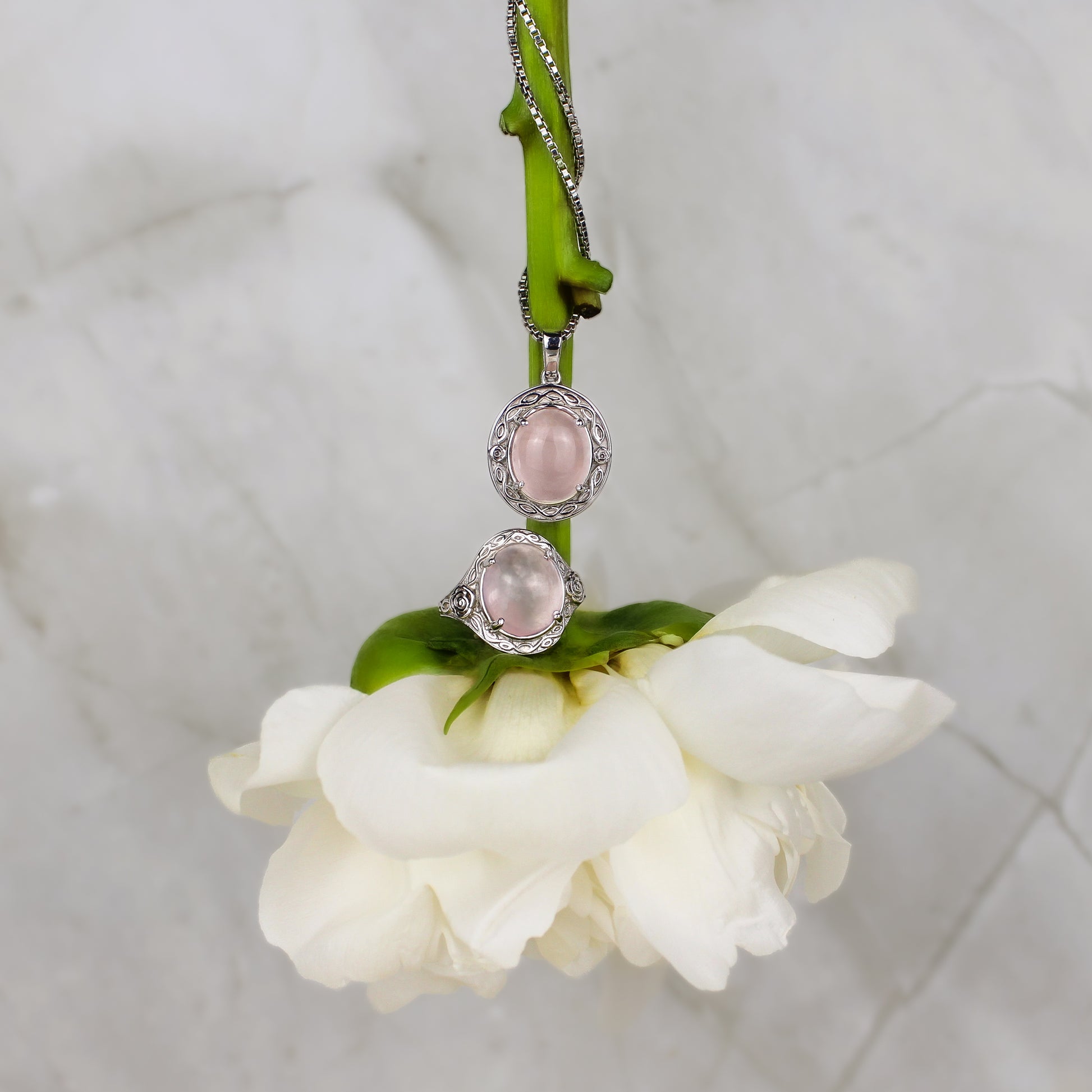 Romantic Heir Necklace and ring with pink gemstones on a white flower against a marble background