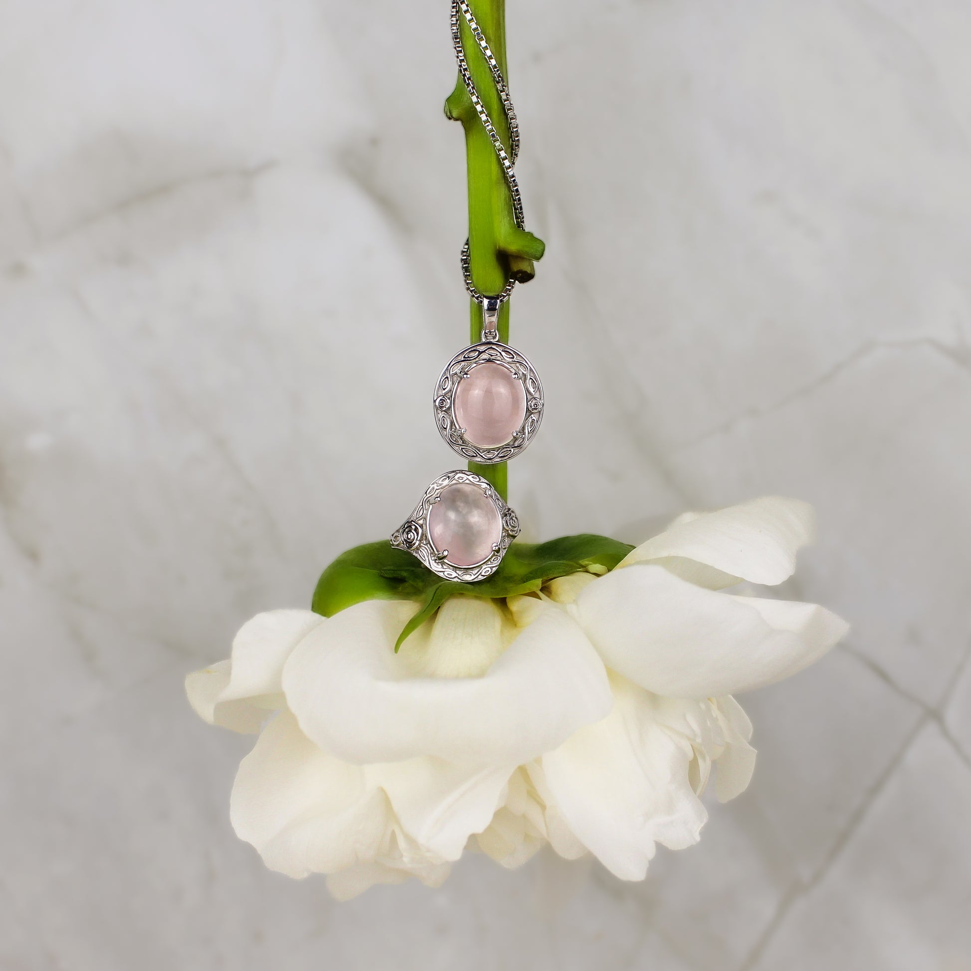 sterling silver romantic heir Necklace and signet ring with pink quartz gemstones and flower engravings on a white flower stem against a marble background