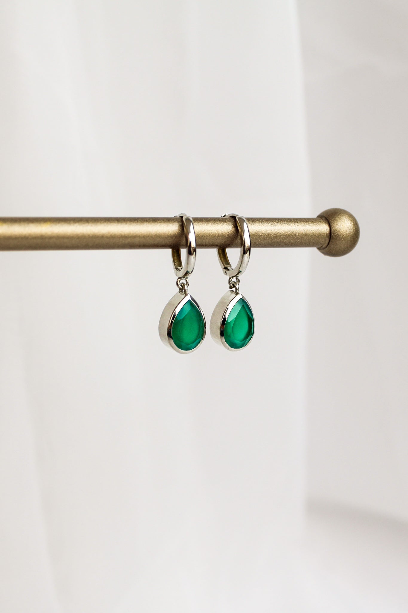 Devoted sterling silver earrings staged on brass jewelry bar display, green onyx teardrop huggie hoop earrings, Ether Jewelry