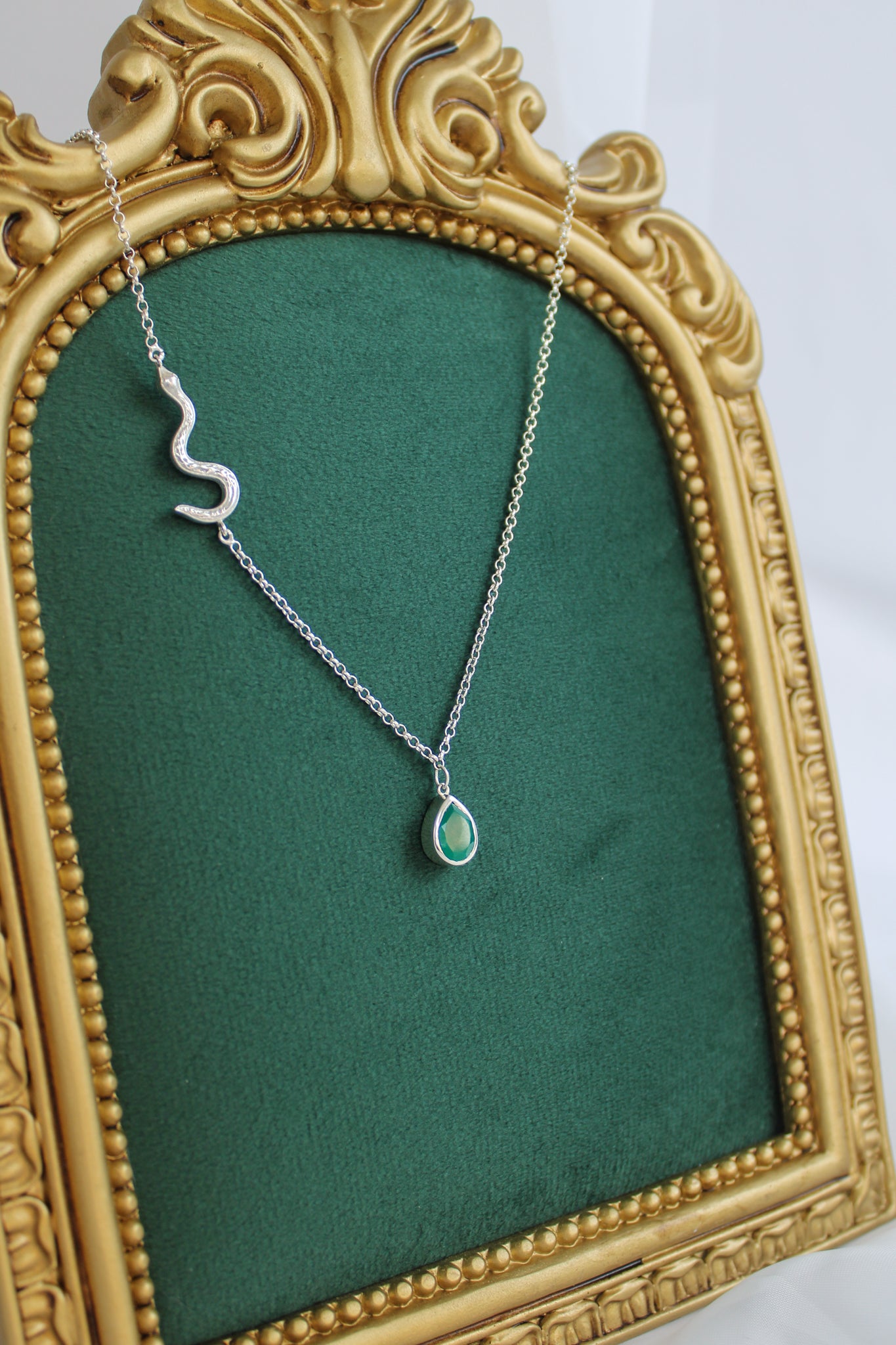 Devoted sterling silver necklace staged on green fabric display, serpent chain with green onyx teardrop pendant, Ether Jewelry