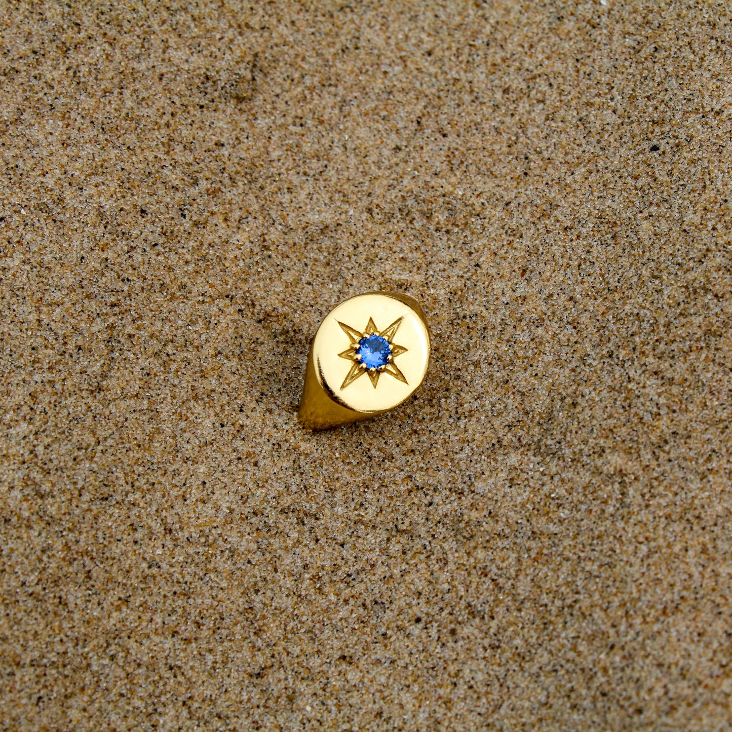 18k gold vermeil Wayfinder Ring staged in sand beach, round north star signet ring with blue CZ center, Ether Jewelry