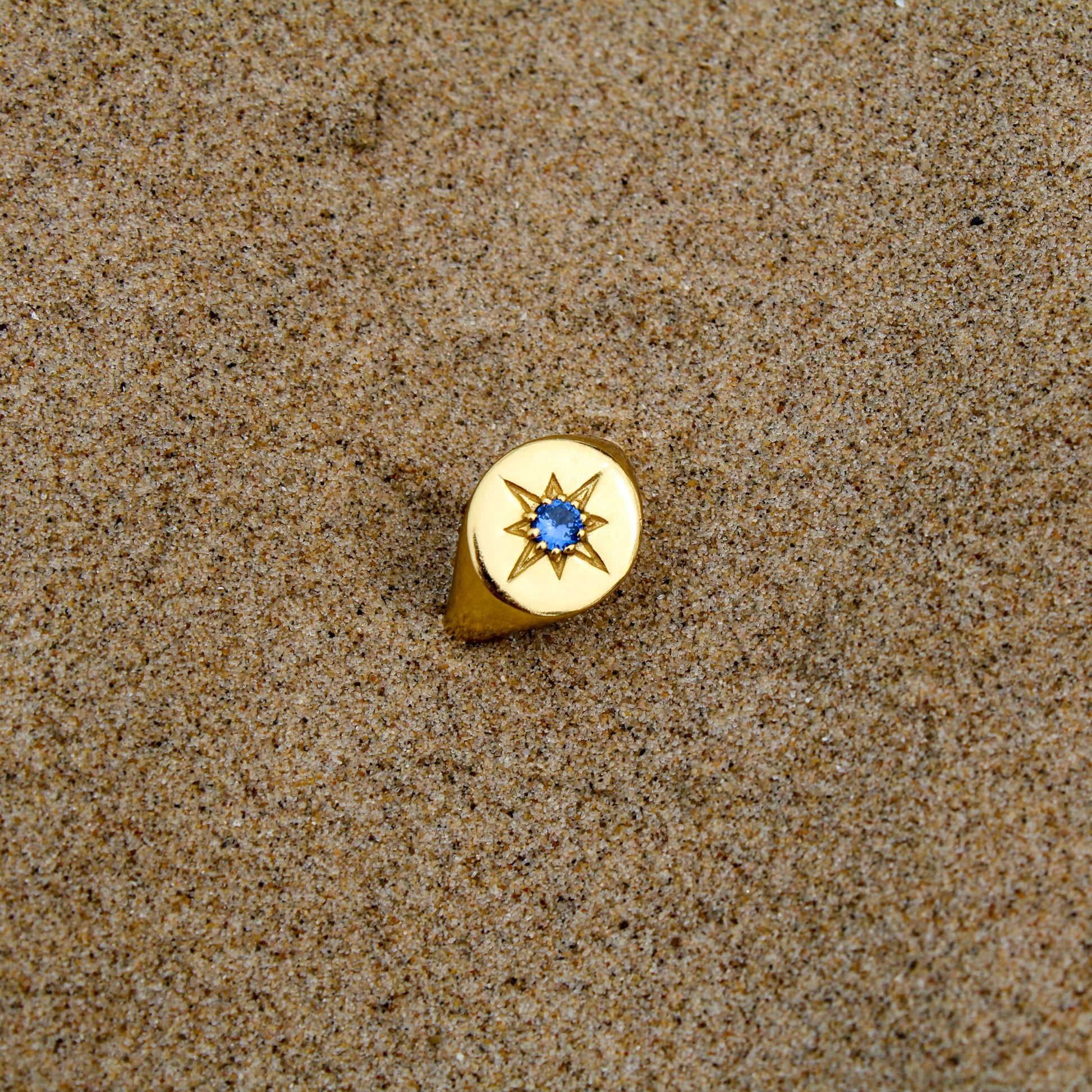 18k gold vermeil Wayfinder Ring staged in sand beach, round north star signet ring with blue CZ center, Ether Jewelry