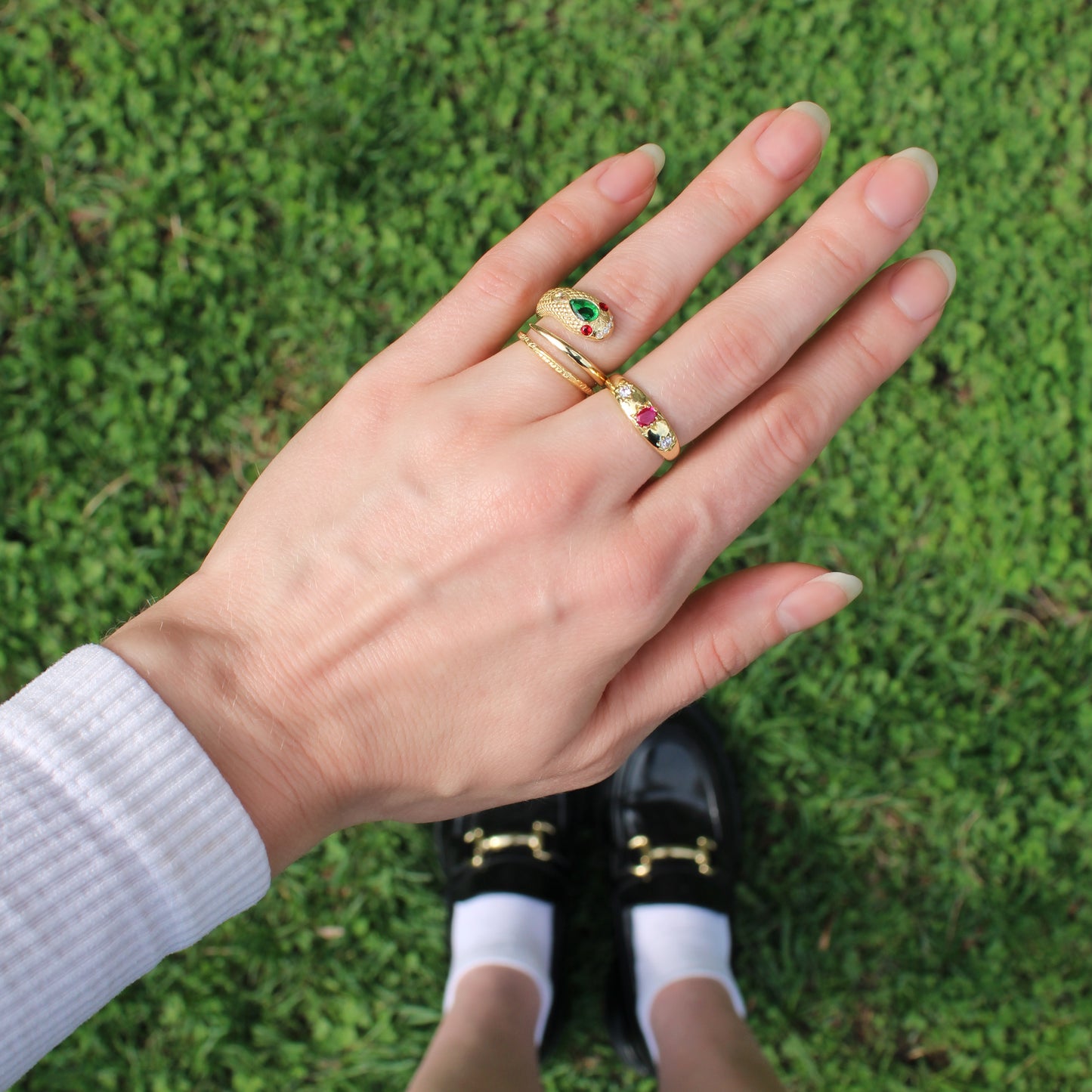 Hand wearing Gold vermeil snake ring and three stone pink Roma Ring on a grassy background, Ether Jewelry.