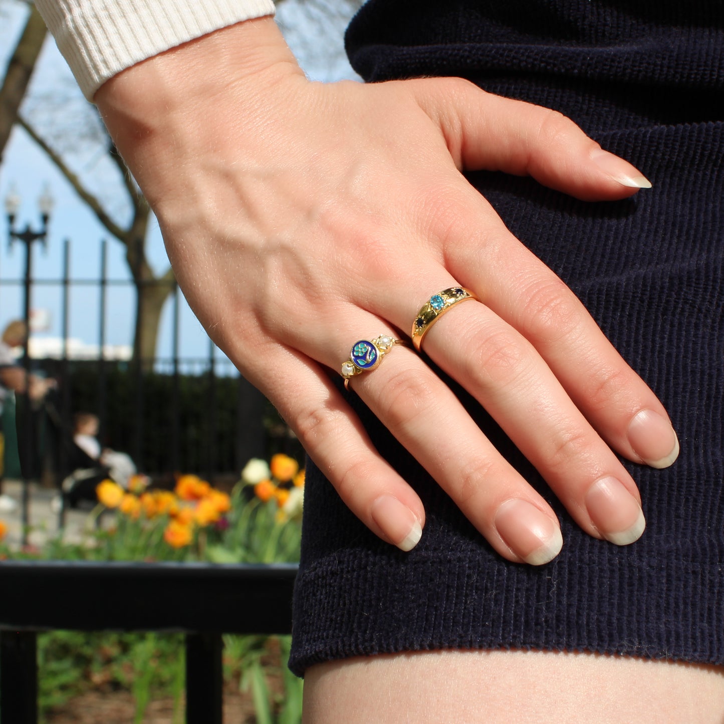 Hand wearing two victorian rings with gemstones and forget-me-not against a blurred park background, Ether Jewelry