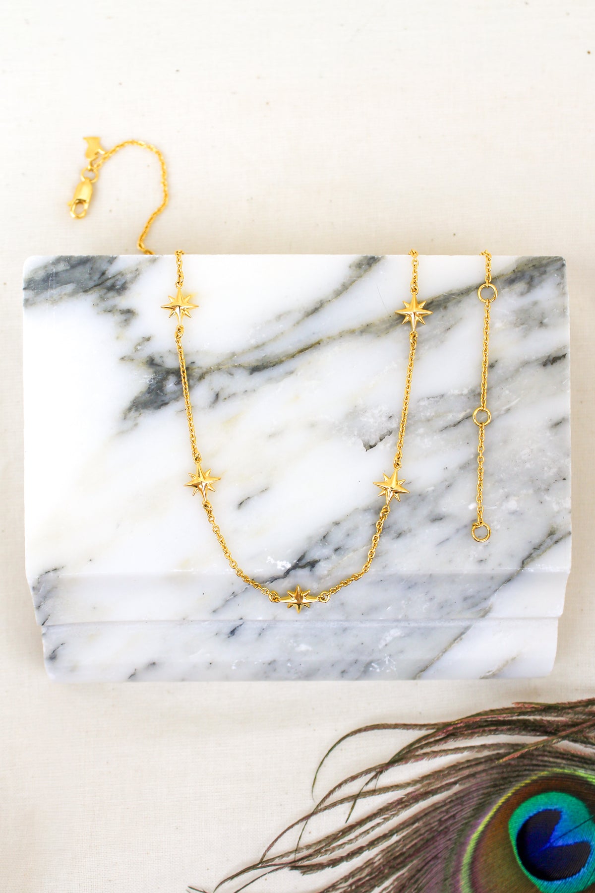 Juno Necklace 18k gold vermeil and sterling silver product photo, staged with peacock feather, multi star charm station necklace, Ether Jewelry