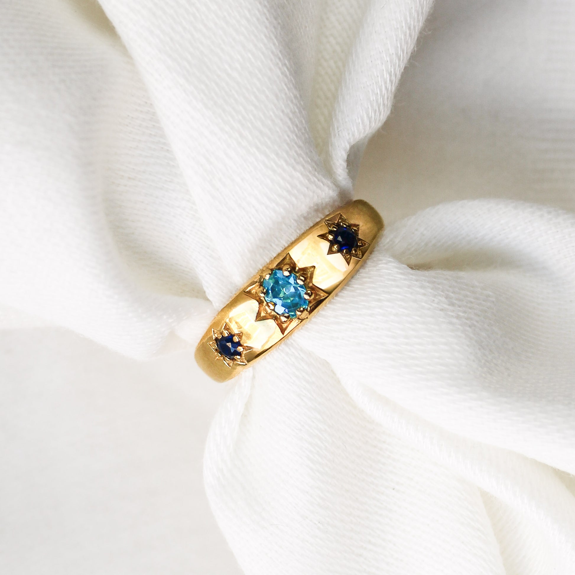 Letters from Roma Ring in 18k gold vermeil, domed gypsy band with light blue CZ center and two star-set blue CZ side stones on white fabric, Ether Jewelry