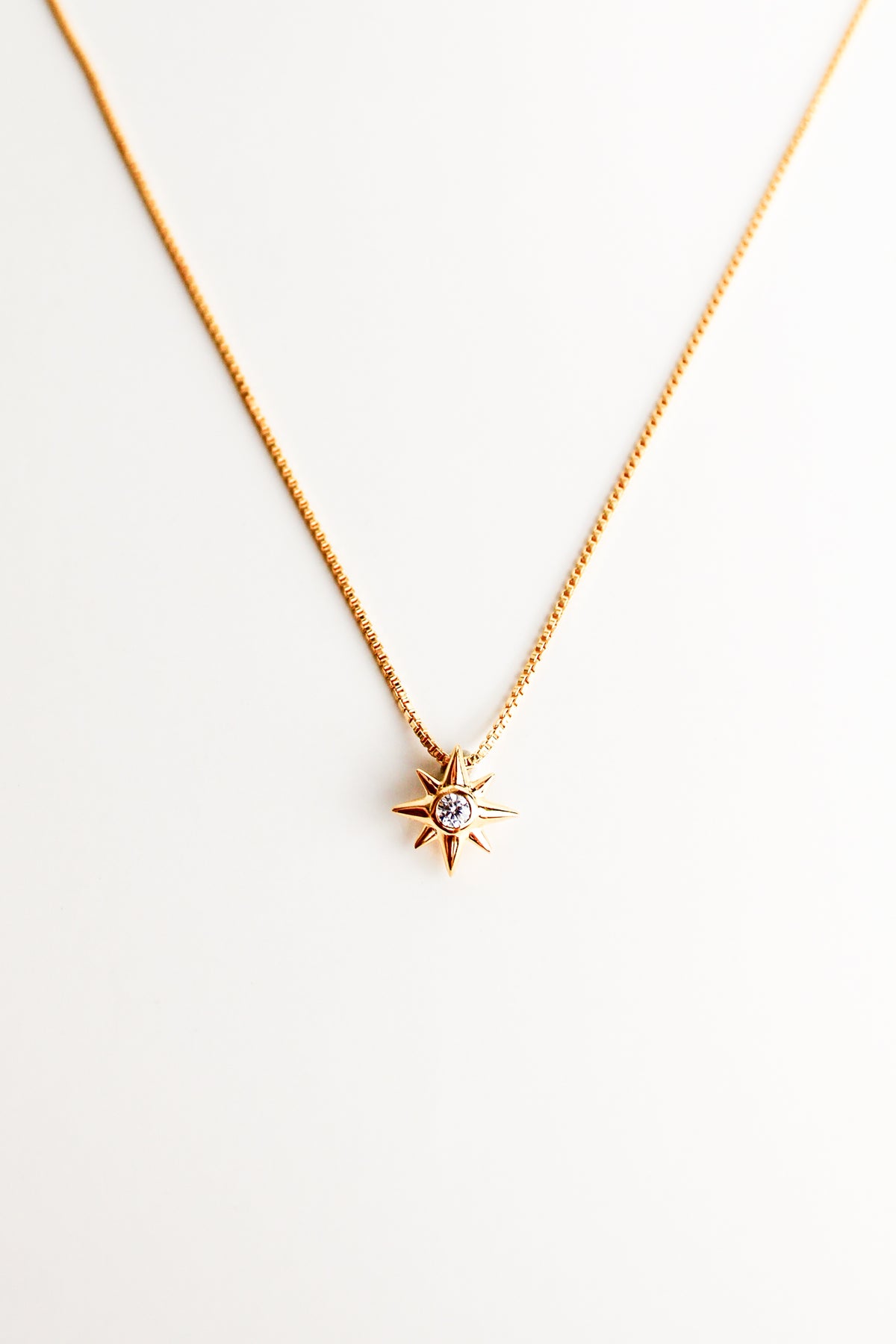 Lucida Necklace against a white background, eight point star pendant on dainty box chain, center cz gemstone, gold vermeil, ether jewelry