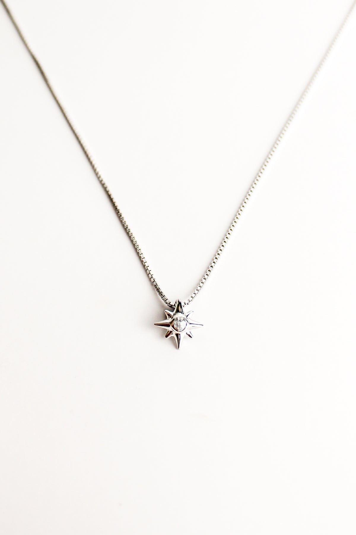 Lucida Necklace against a white background, eight point star pendant on dainty box chain, center cz gemstone, sterling silver, ether jewelry