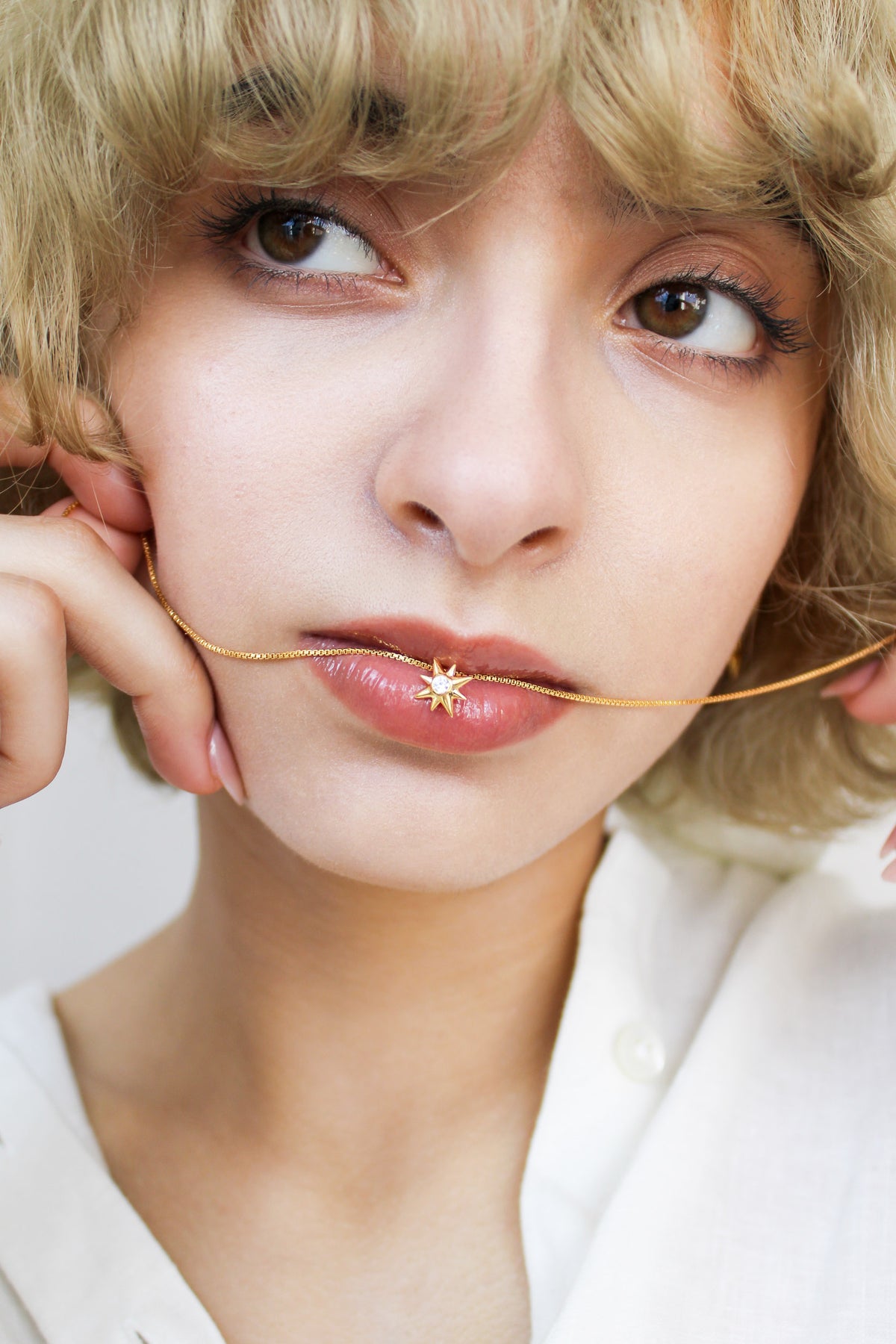 Lucida Necklace in 18k gold vermeil held on models lip, dainty north star CZ pendant on box chain, Ether Jewelry