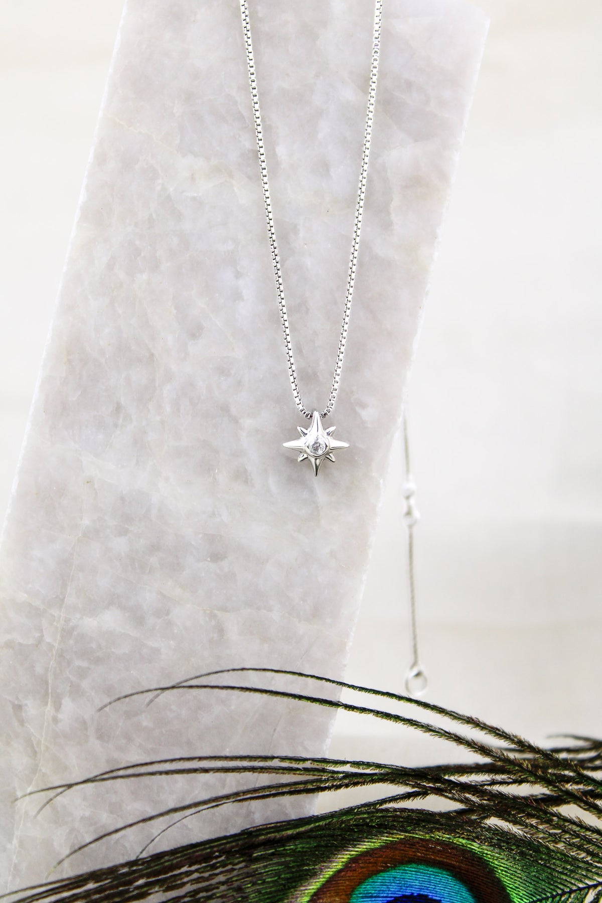 Lucida Necklace 18k sterling silver product photo, north star CZ pendant necklace, on marble with peacock feather, Ether Jewelry