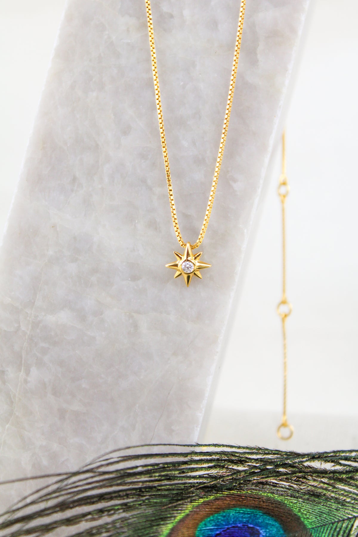 Lucida Necklace 18k gold vermeil and sterling silver product photo, north star CZ pendant necklace, on marble with peacock feather, Ether Jewelry