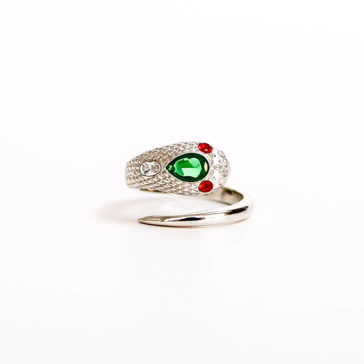 Queen Victoria Ring in sterling silver featuring a prominent green pear gemstone in the center, accented by two small red round gemstones and a clear round stone on the textured scales, set against a plain white background, ether jewelry