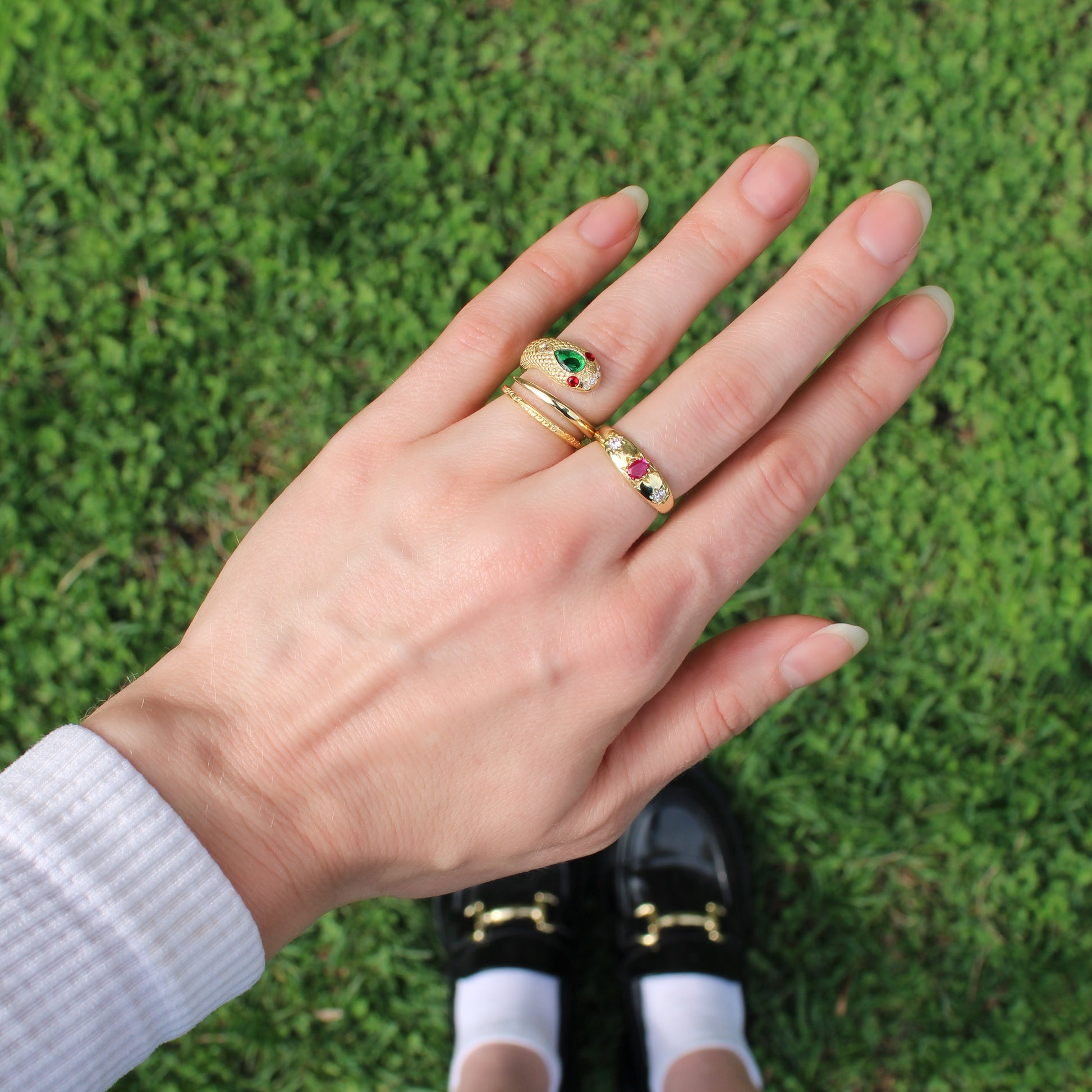 Hand wearing Gold vermeil snake ring and three stone pink rose from Roma Ring on a grassy background, Ether Jewelry.