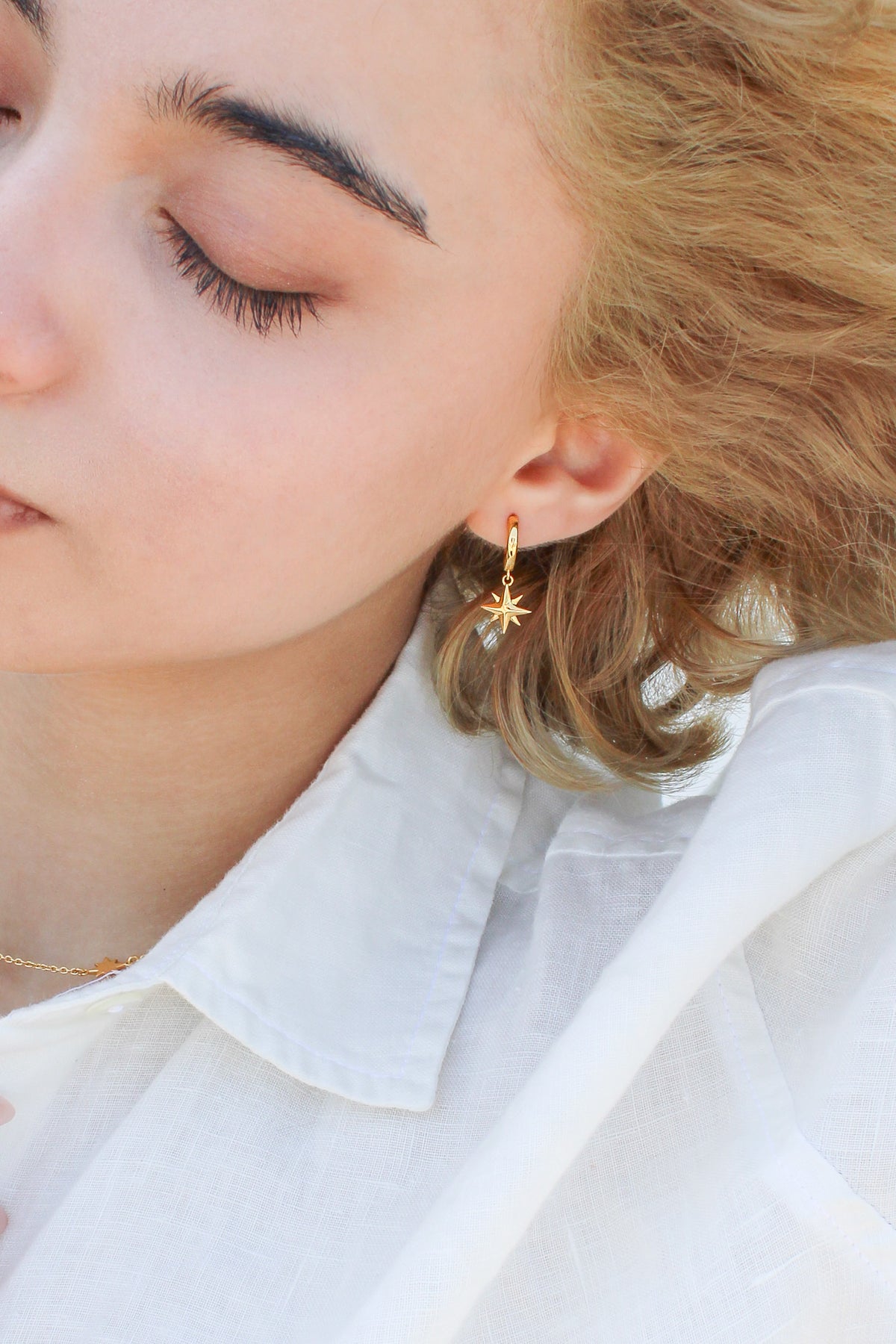 Stella Hoops in 18k gold vermeil on model with hair blowing in wind, solid north star charm drop huggie hoops, Ether Jewelry