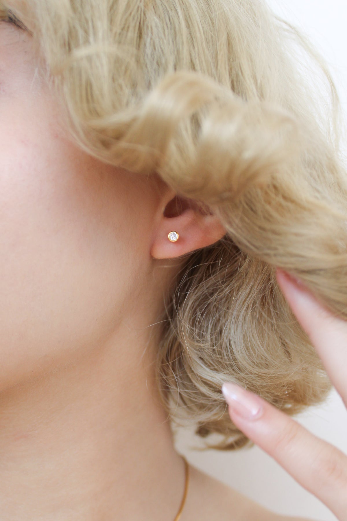 18k gold vermeil Vesta Stud Earrings on model pushing hair away to reveal earring, bezel CZ stud earring, Ether Jewelry