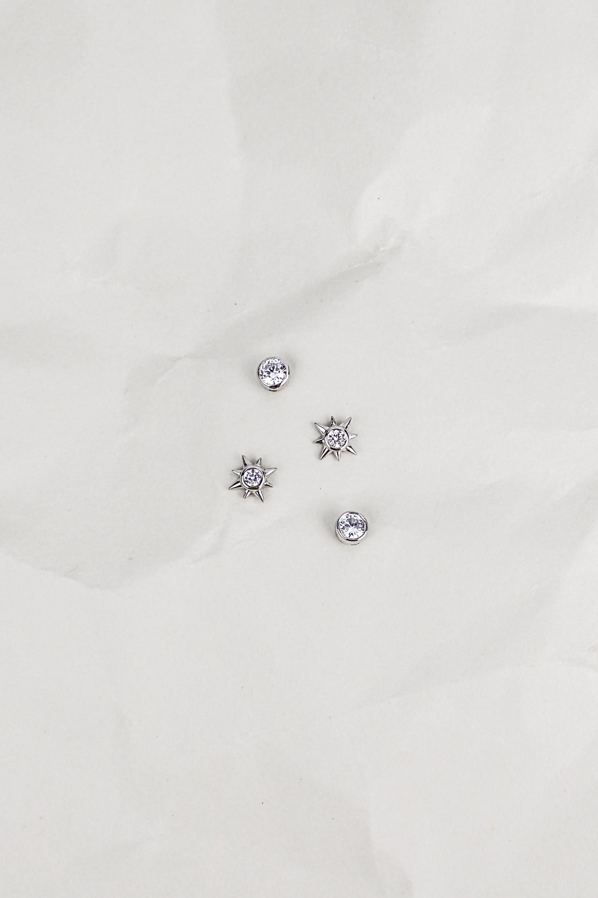 Stella Stud Earrings in sterling silver staged on crinkled paper, dainty north star CZ stud earrings, Ether Jewelry