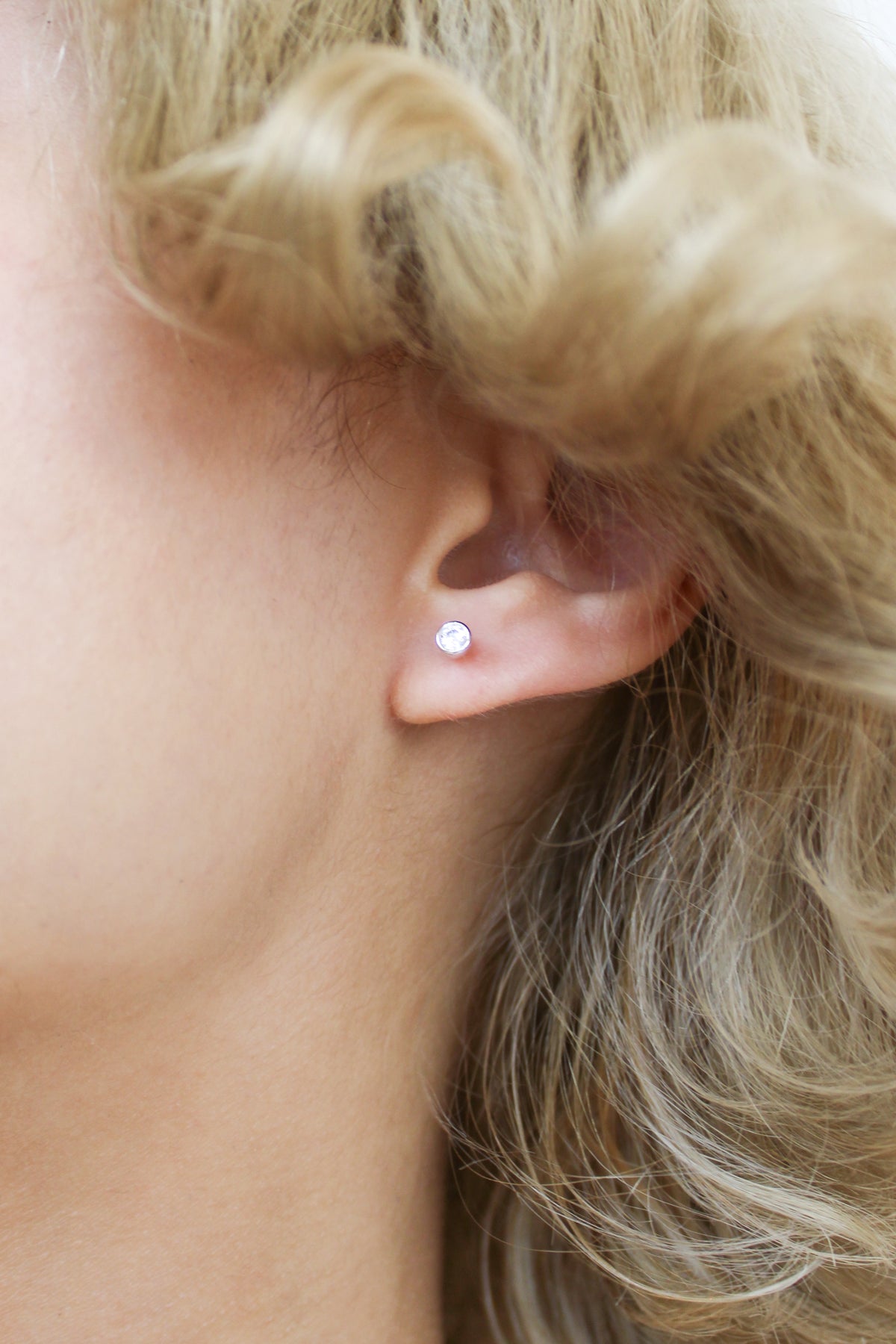 Sterling silver Vesta Stud Earrings close-up on model ear, bezel-set round CZ stud earring detail, Ether Jewelry