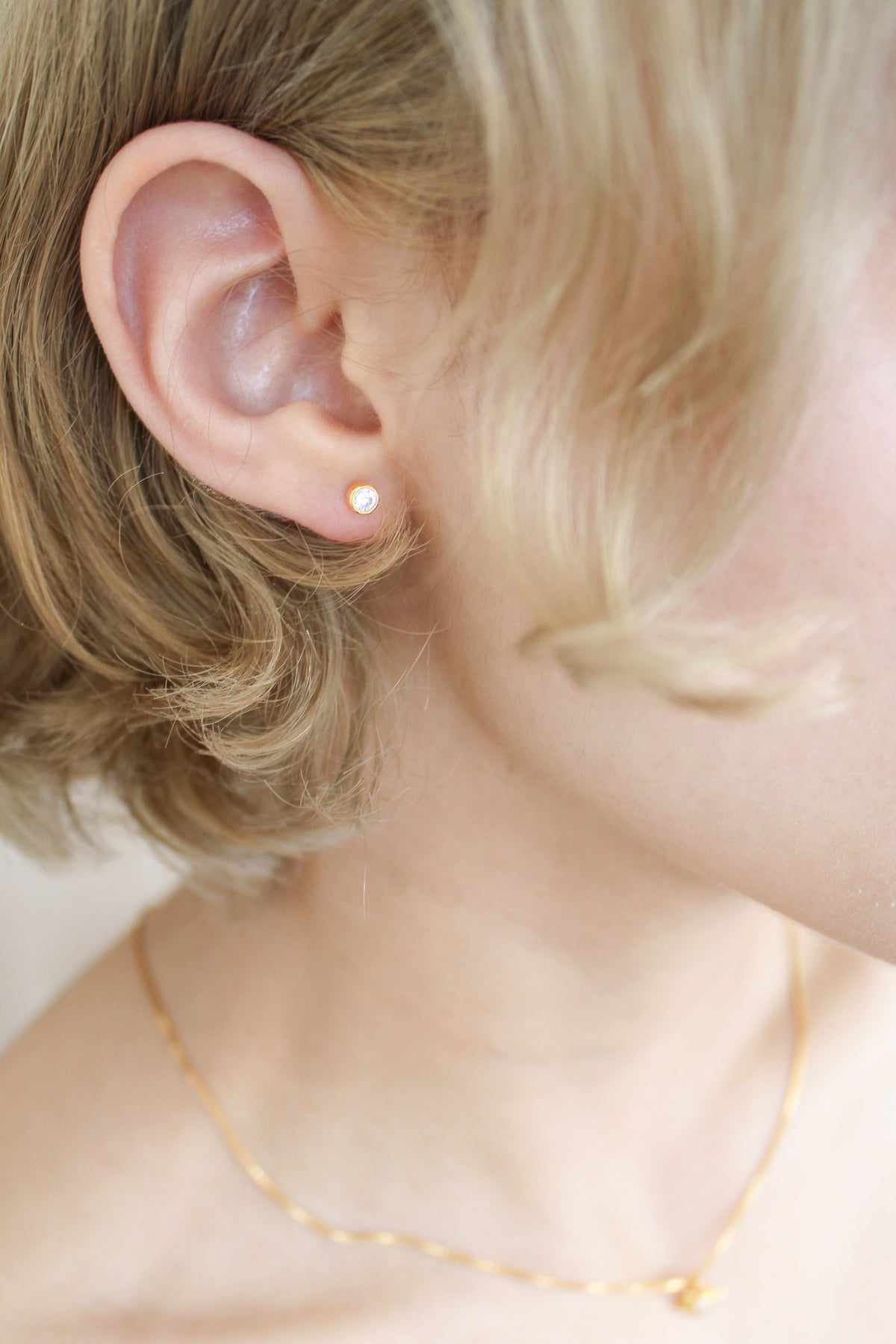 Vesta Stud Earrings in 18k gold vermeil on model, dainty bezel-set round CZ stud earrings, Ether Jewelry
