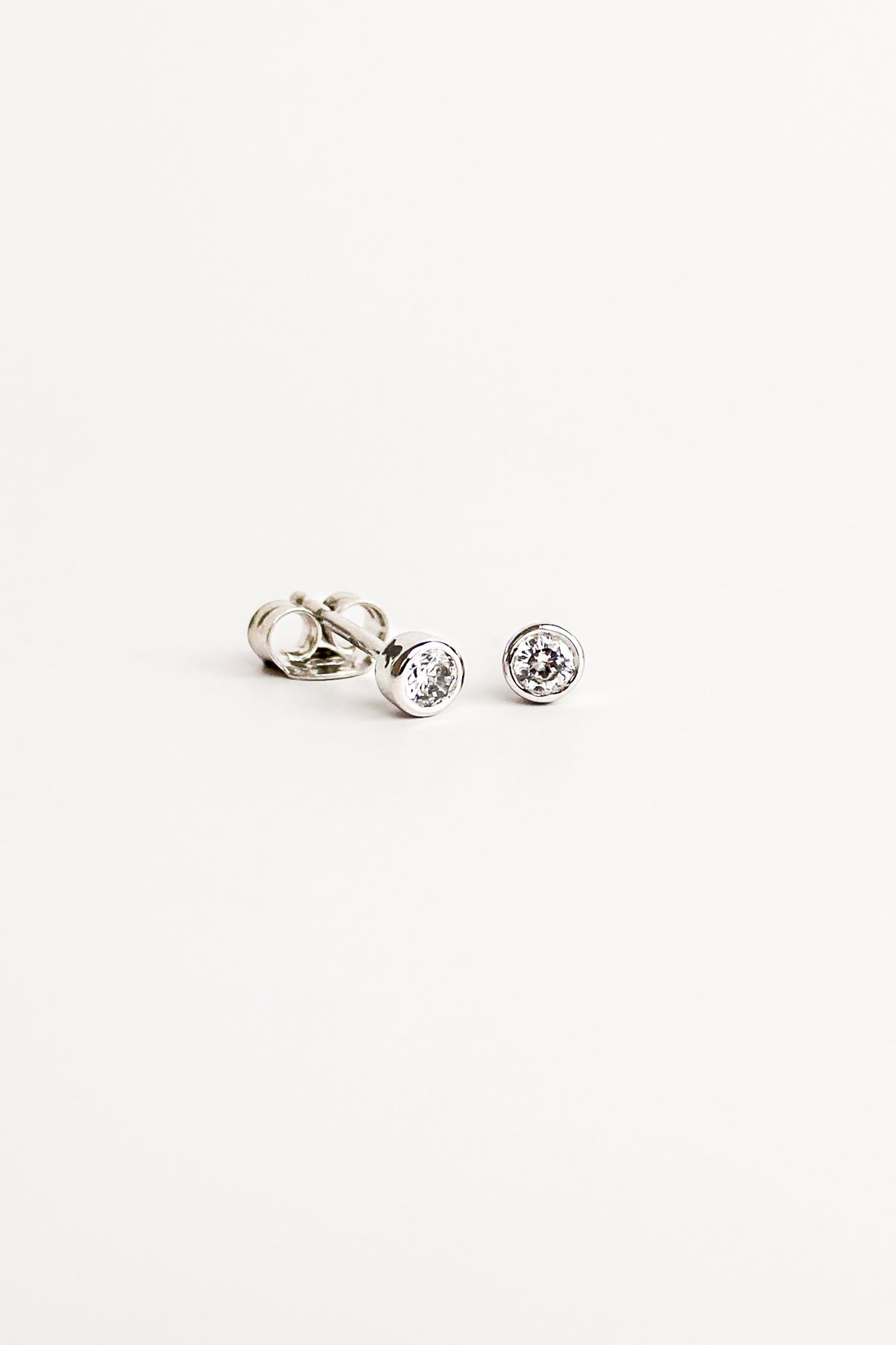 Vesta Stud Earrings in sterling silver, dainty bezel-set round CZ stud earrings, white background, Ether Jewelry