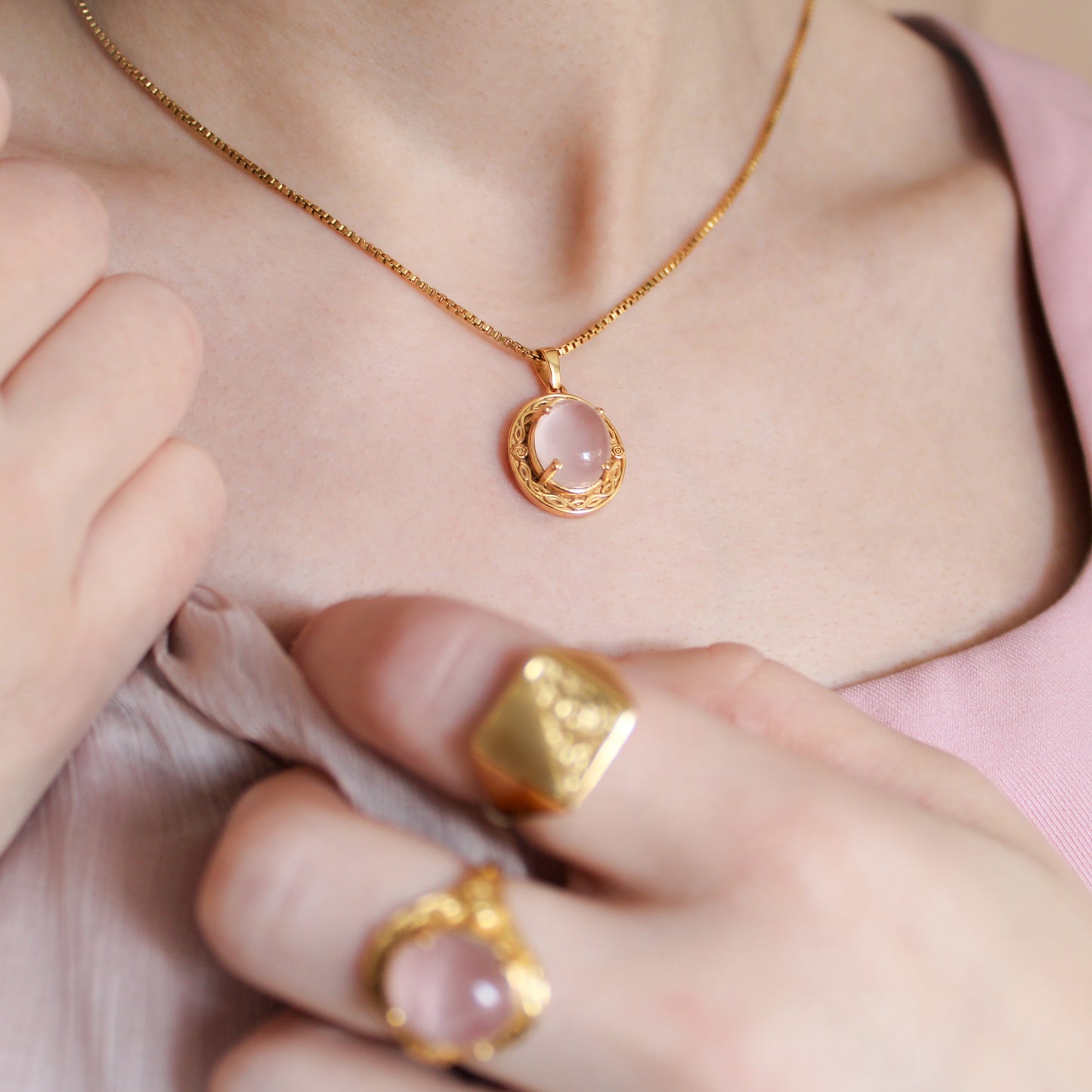 Close-up of a person wearing Romantic Heir gold necklace with a pink stone pendant and matching rings.
