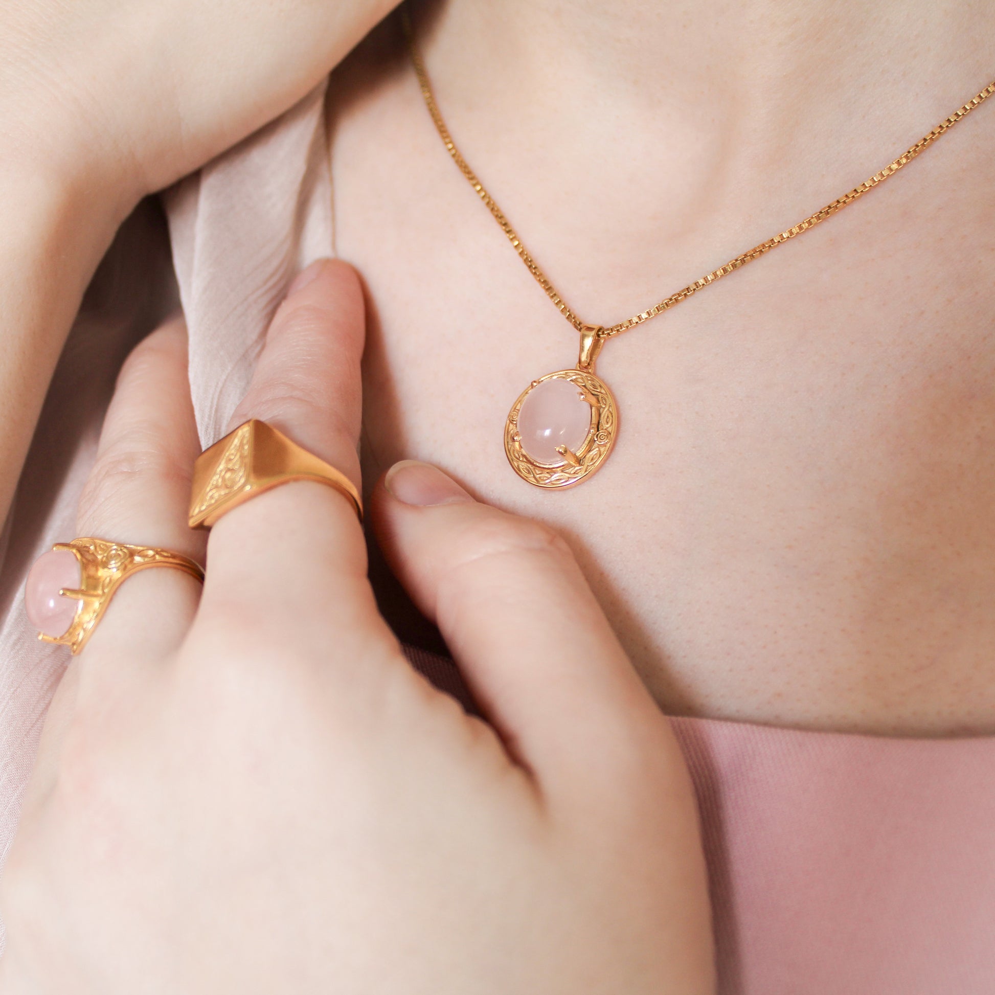 Gold Romantic Heir necklace with a pink quartz stone pendant worn by a person, with gold rings on fingers.