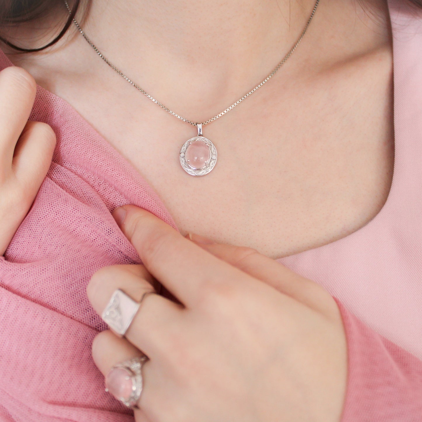 Person wearing a sterling silver Romantic Heir  necklace with a pink pendant, close-up on neck and hand.