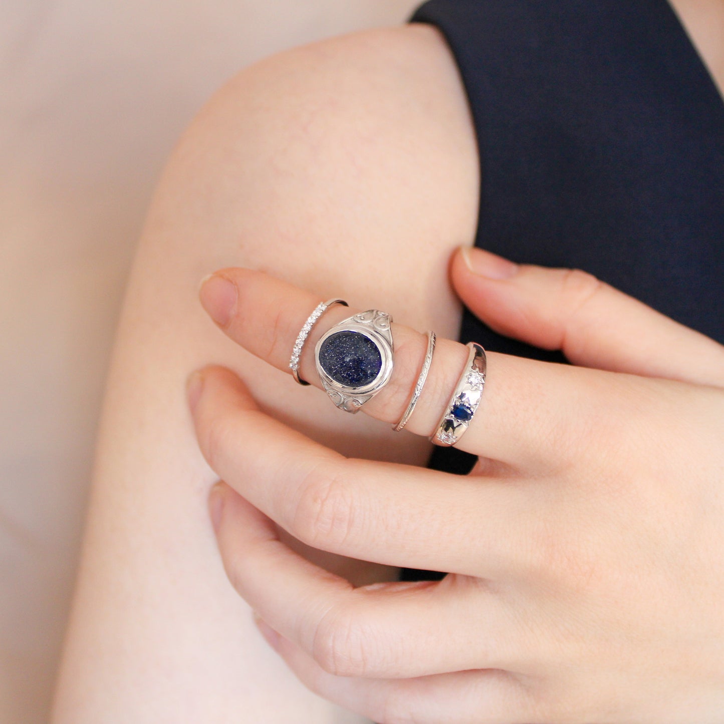 Close-up of a hand wearing multiple sterling silver rings and night keeper signet ring with blue sandstone gemstone on a light background
