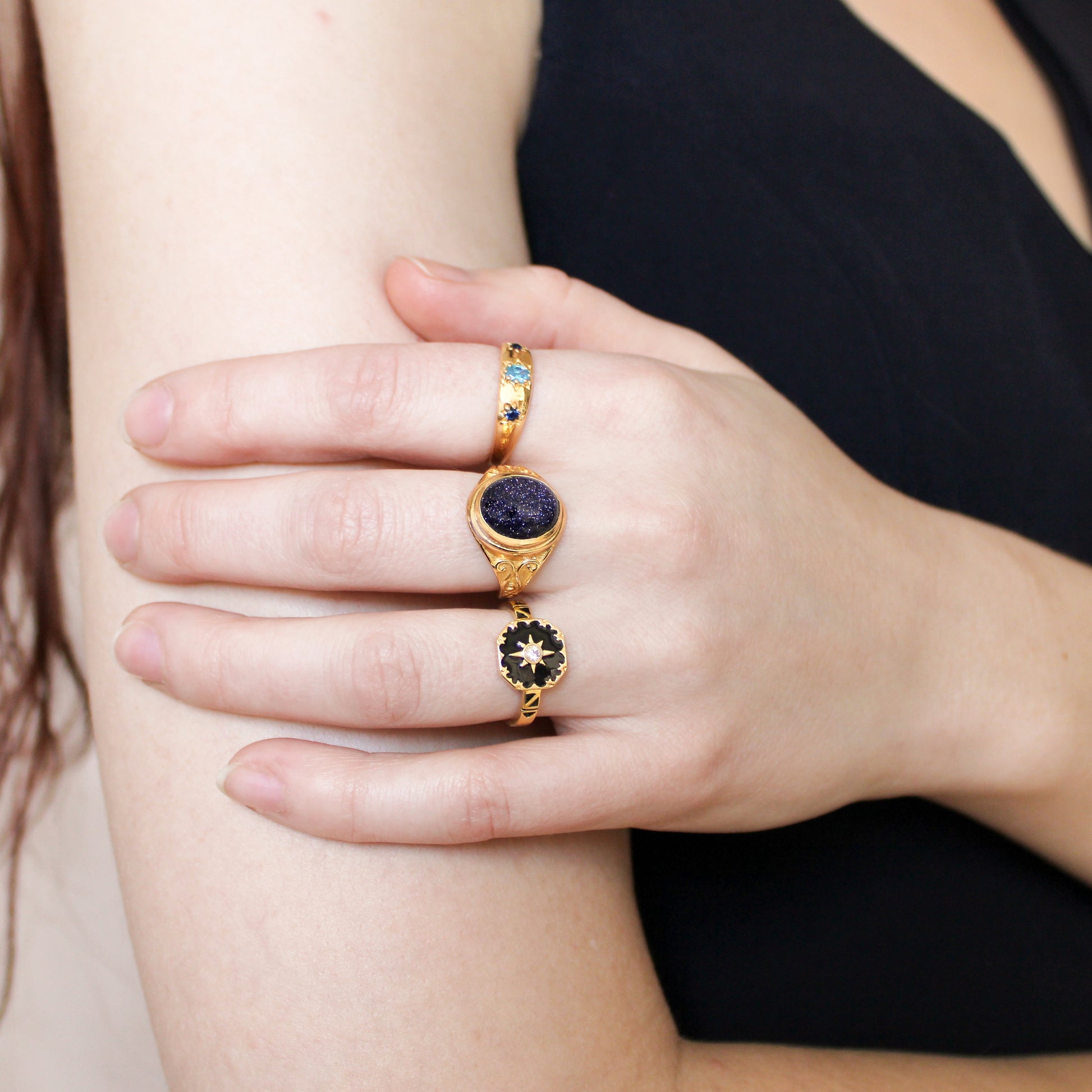 Close-up of a hand wearing three gold rings with gemstones on a neutral background
