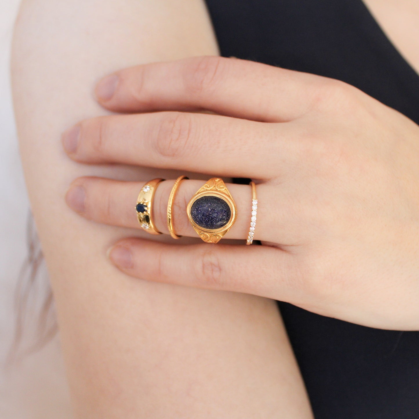 model Hand wearing gold night keeper signet ring and stacker rings with blue sandstone gemstones on a light background