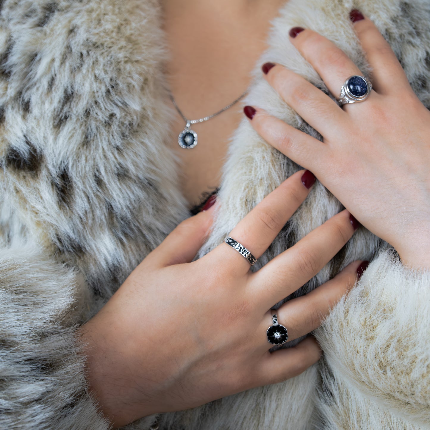 Close-up of hands wearing blue sand stone signet rings in a fur coat