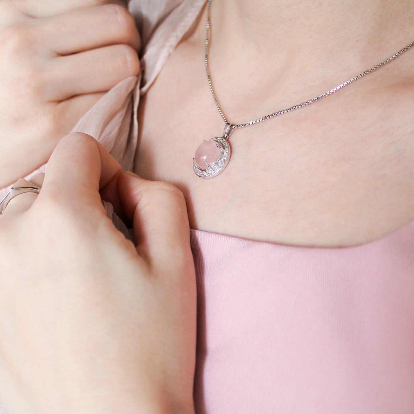 Person wearing Romantic Heir necklace with a pink quartz pendant, set against a soft pink background
