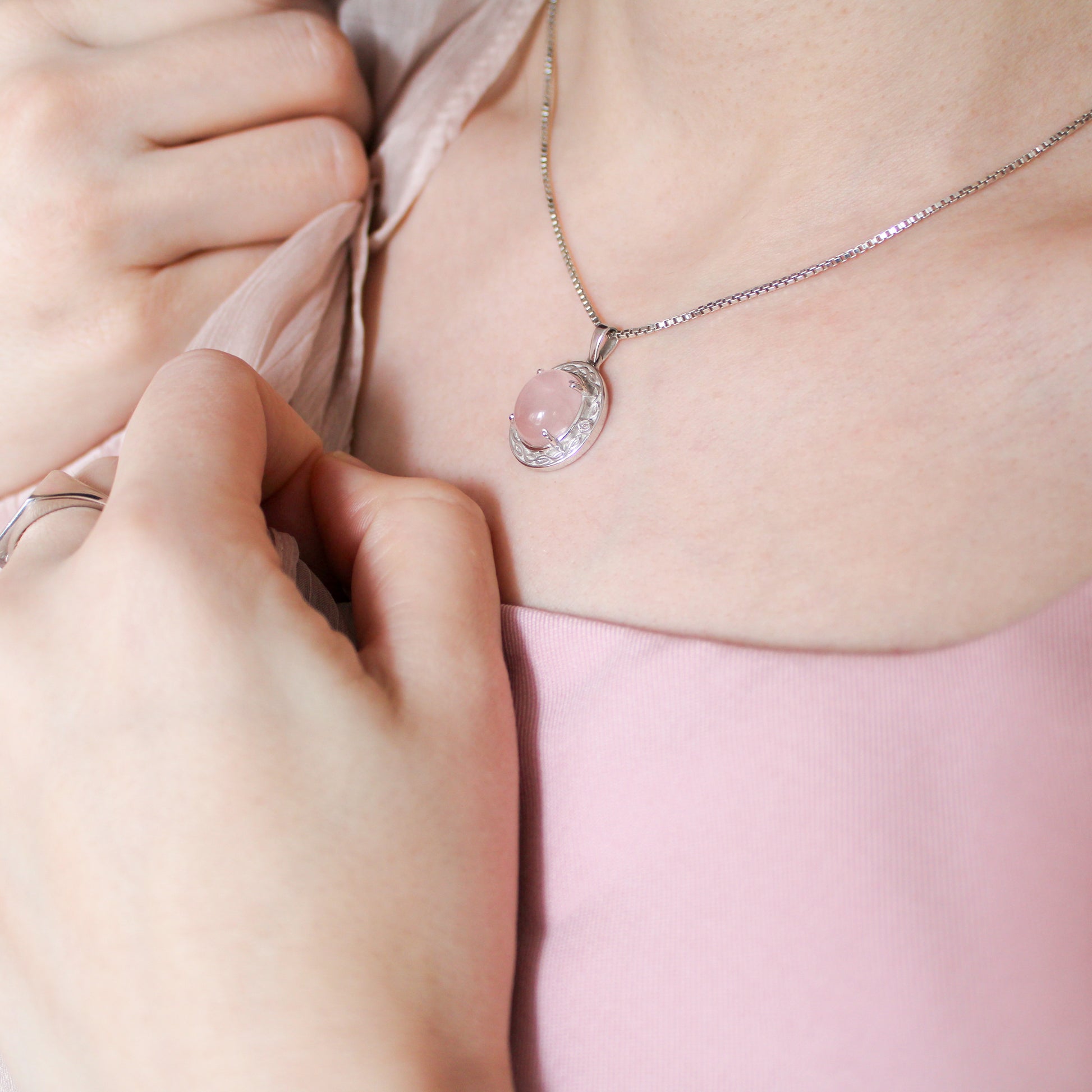 Person wearing Romantic Heir necklace with a pink quartz pendant, set against a soft pink background