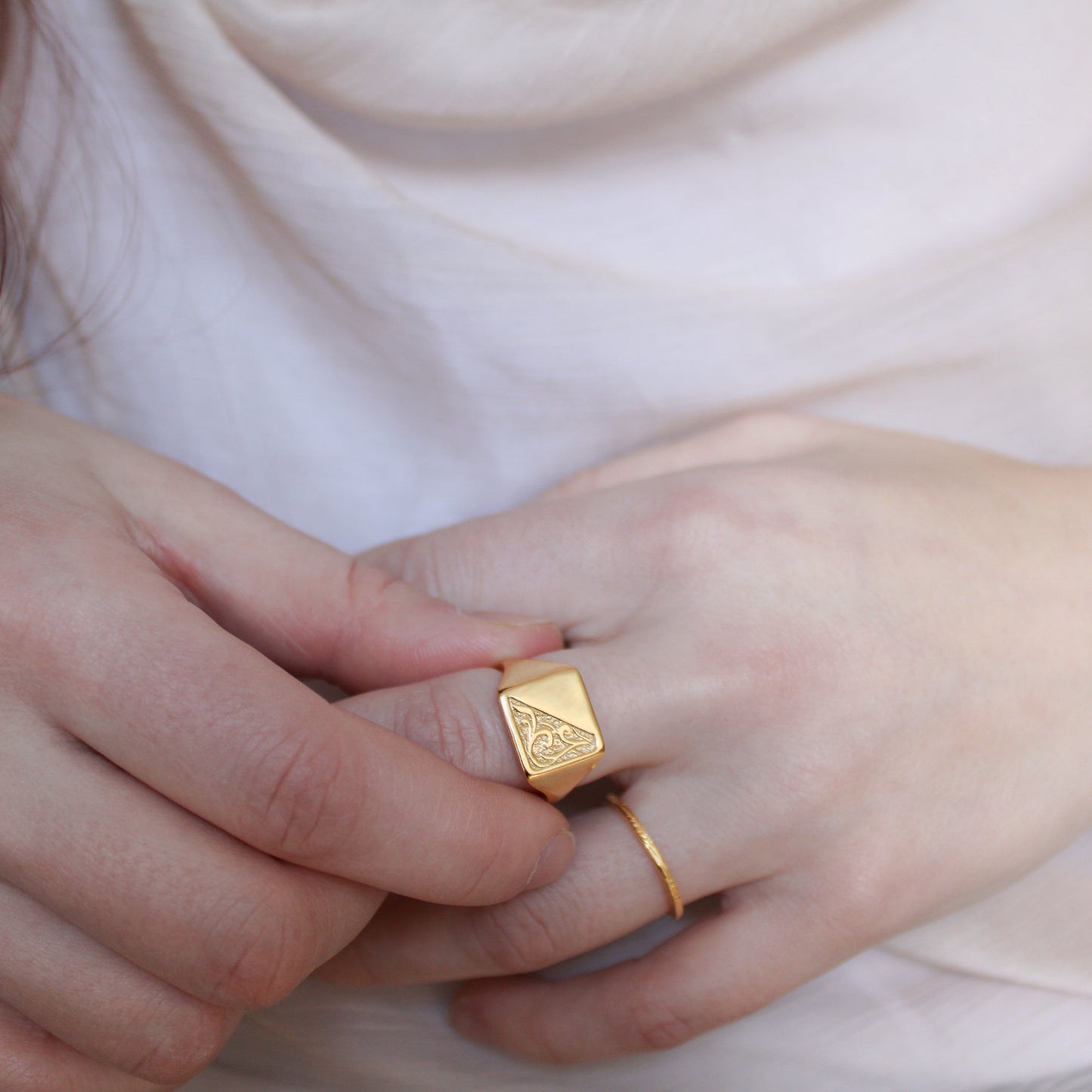 Gold architect signet square ring on a finger with a soft background
