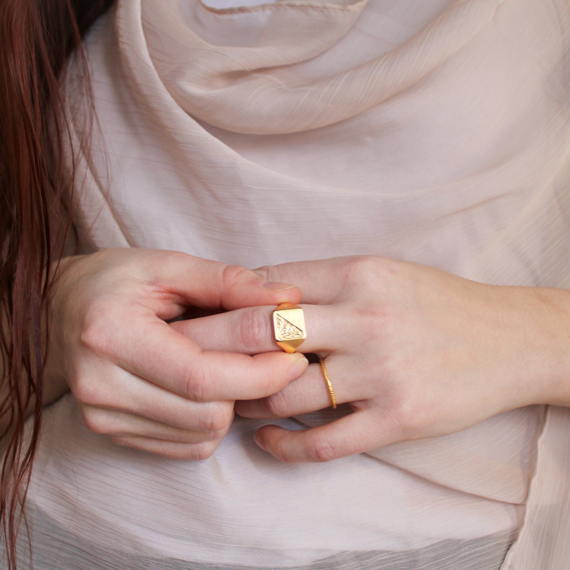 Close-up of hands wearing gold signet rings with a soft, neutral background