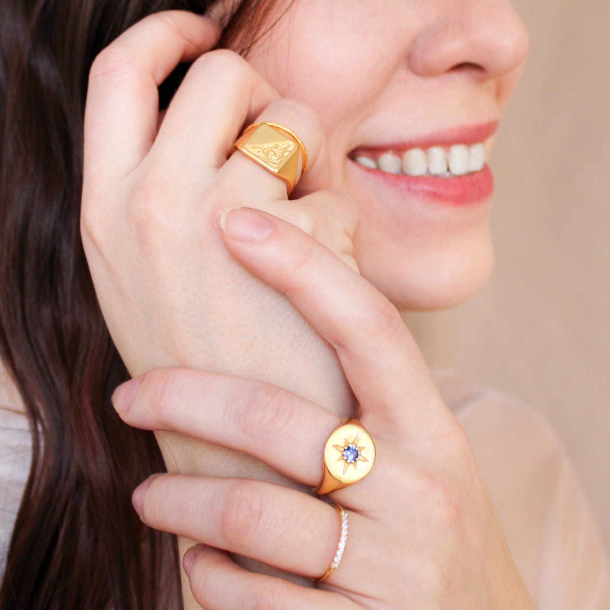 Close-up of a woman's hand wearing two gold signet rings with gemstones.