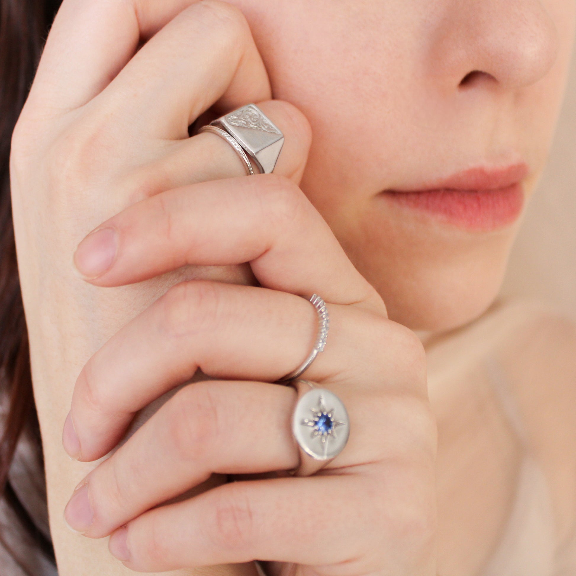 Close-up of a person's hand wearing two sterling silver signet rings with gemstones.