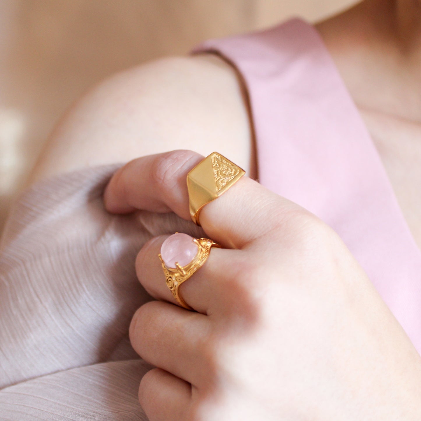 Gold signet rings on a person's fingers with a soft background