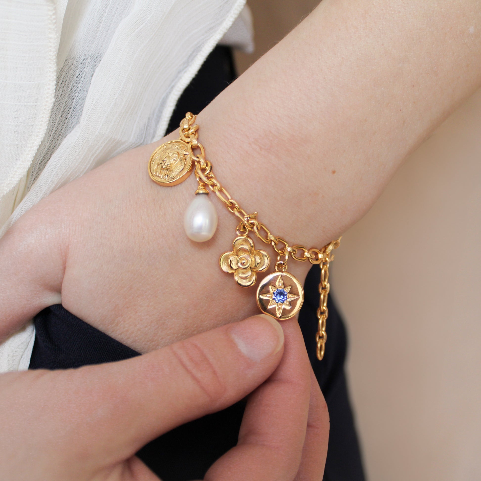 Gold archivist bracelet with charms on a wrist against a neutral background